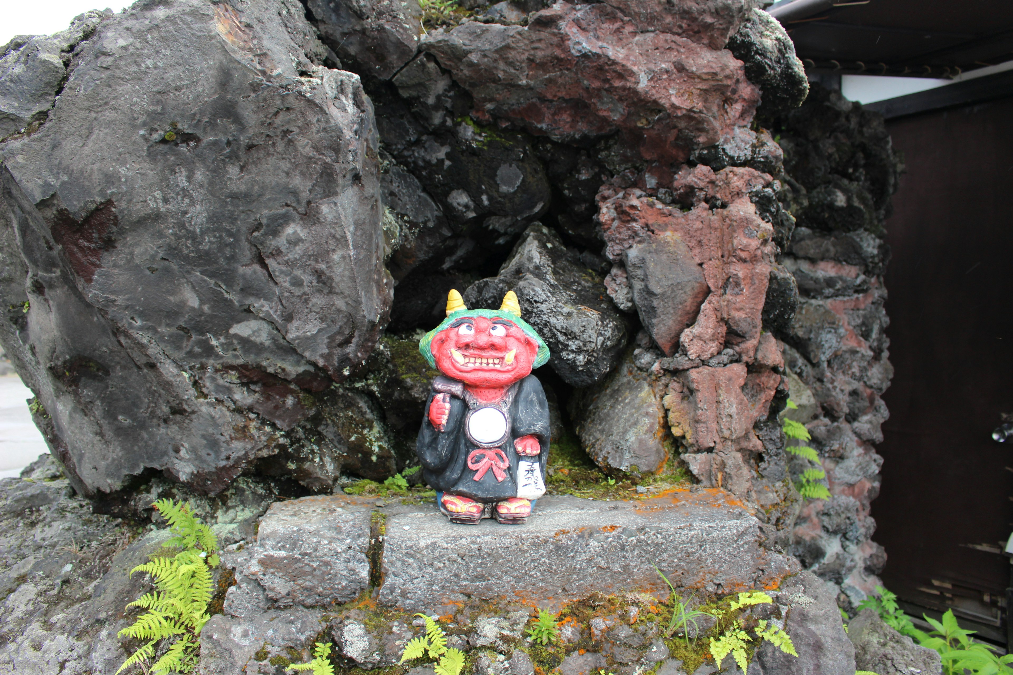 A red demon statue placed among rocks with green plants