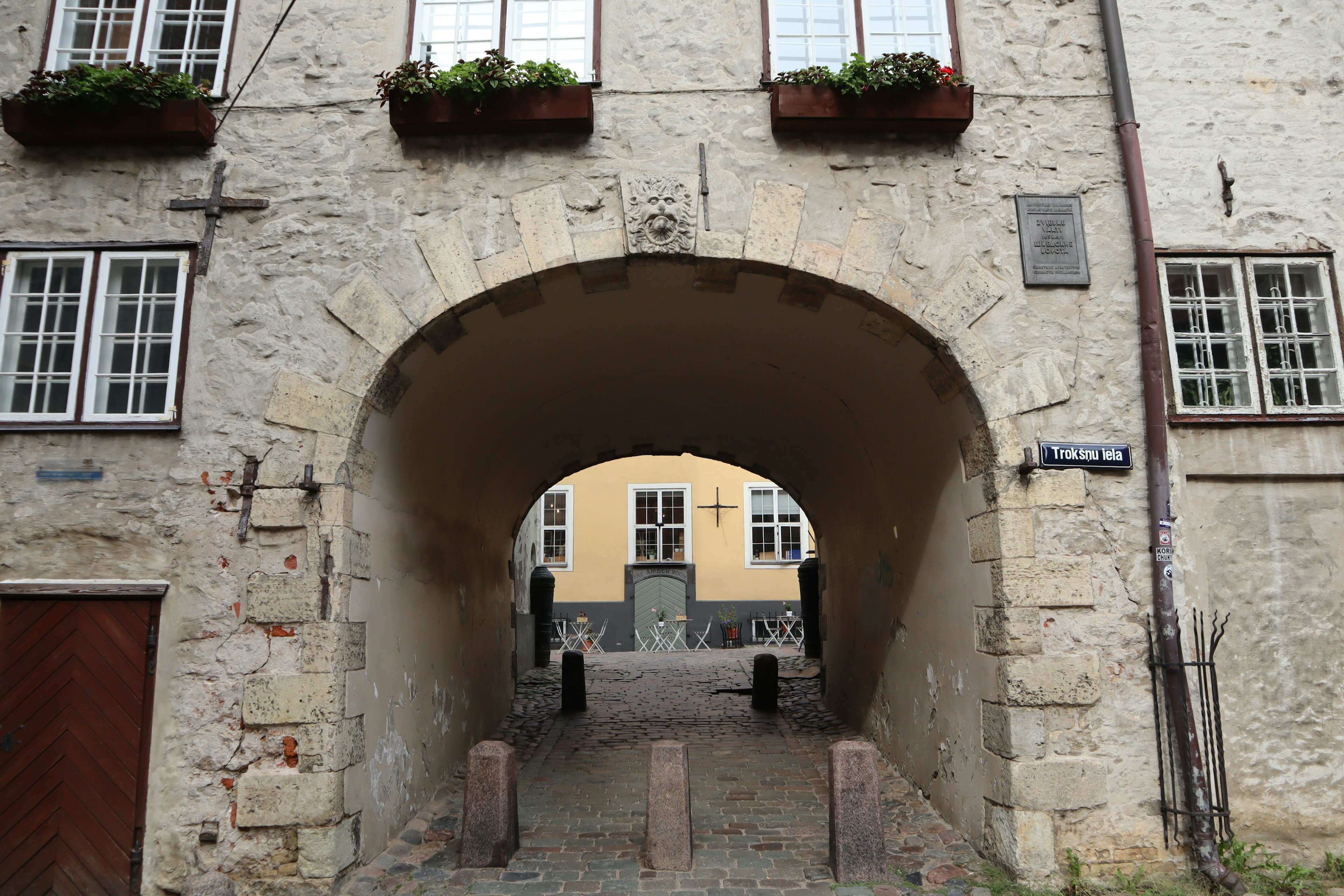 Arco de piedra con edificios visibles al fondo y macetas de flores