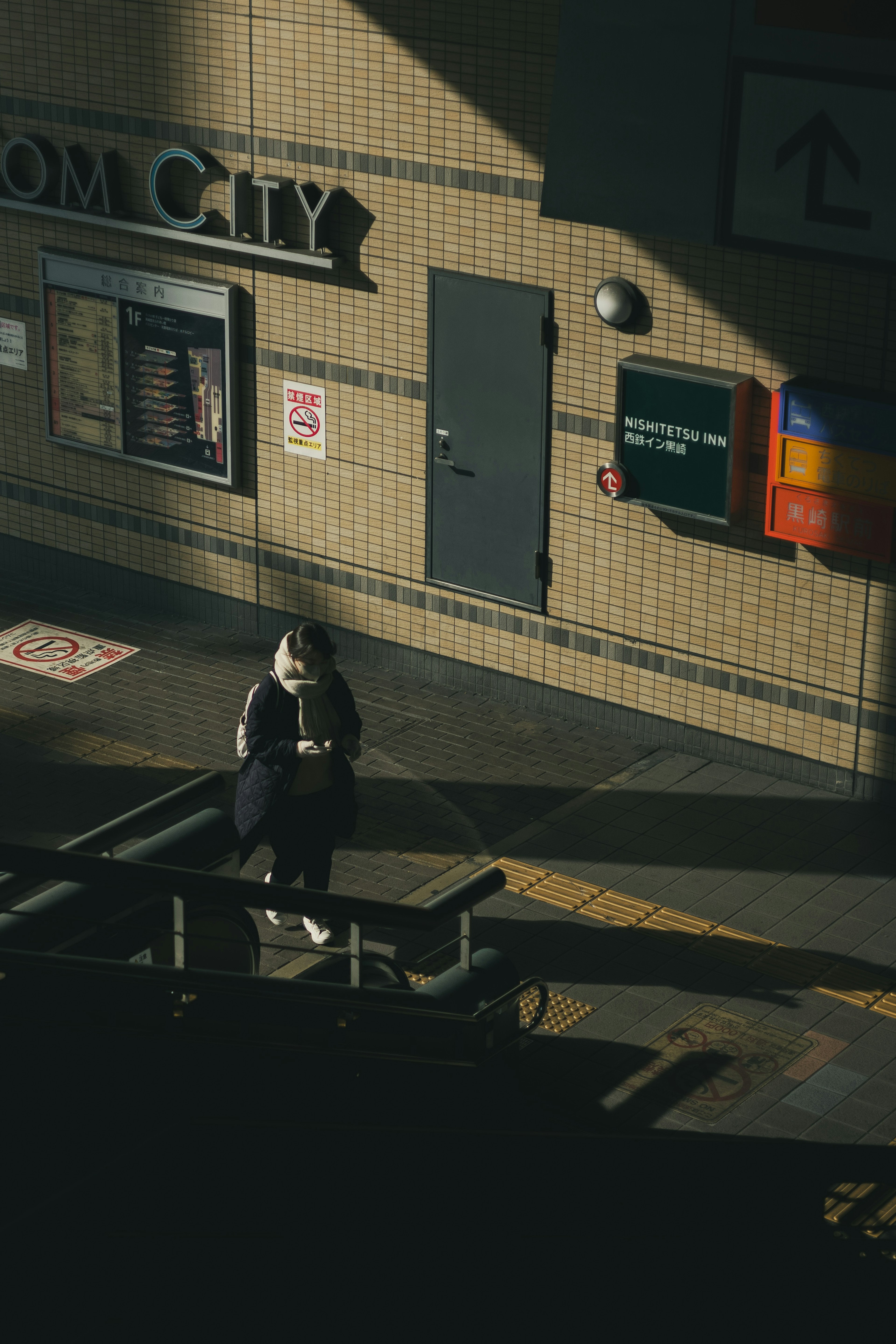 Eine Person wartet auf einem Bahnsteig mit kontrastierenden Licht- und Schattenverhältnissen