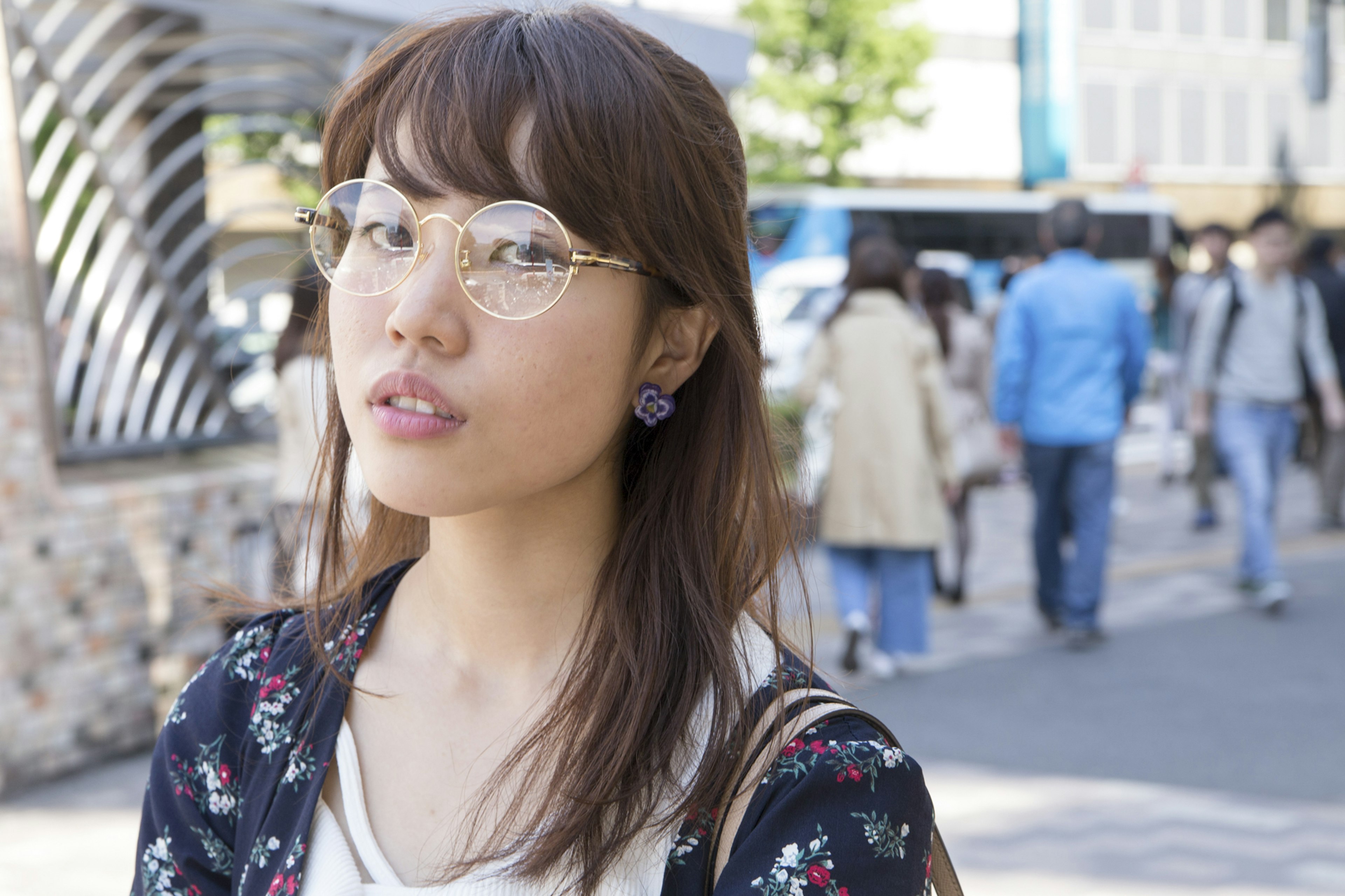 A young woman wearing glasses stands on a busy street