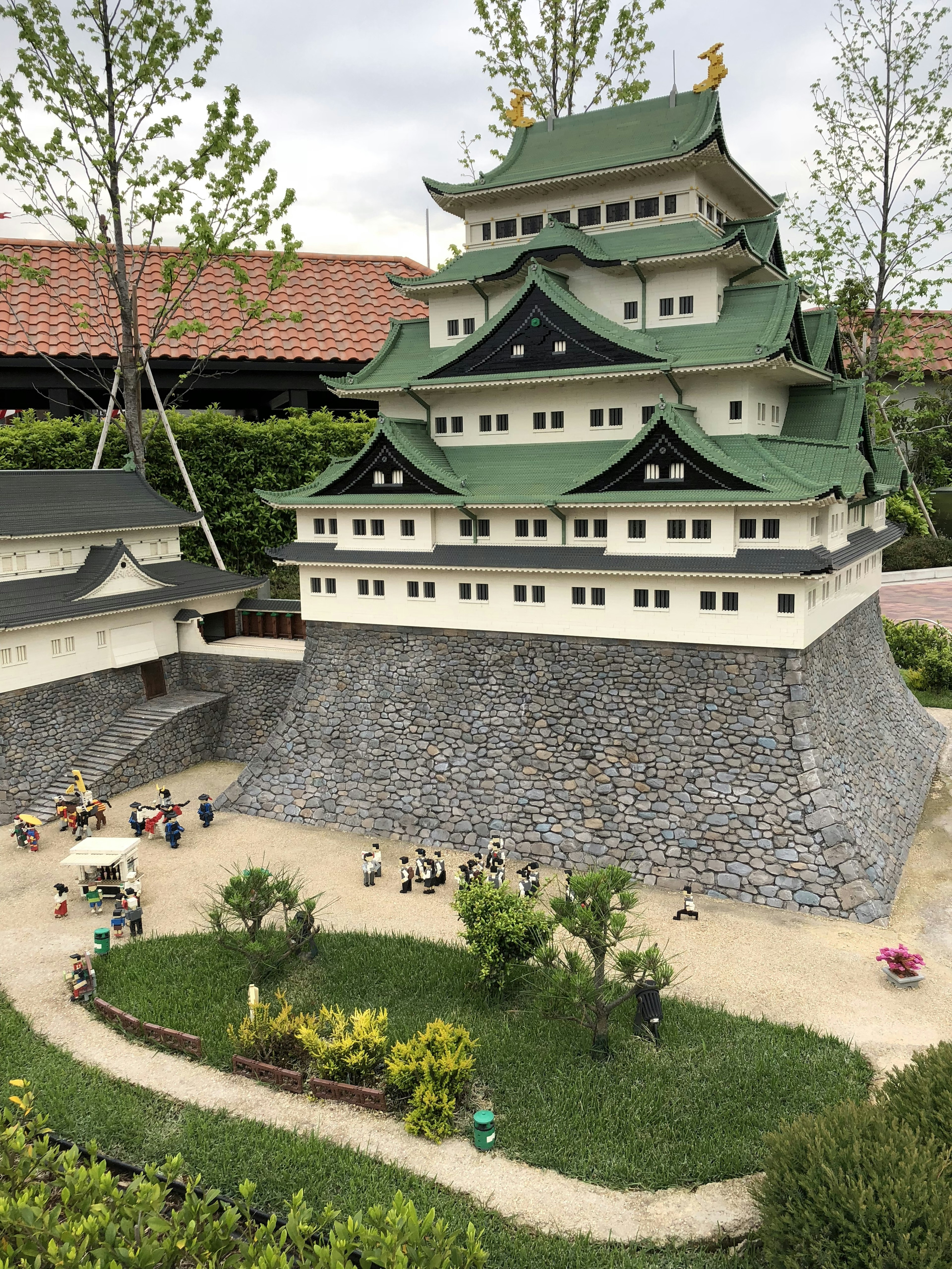 Miniature model of a Japanese castle with green roof surrounded by small figurines