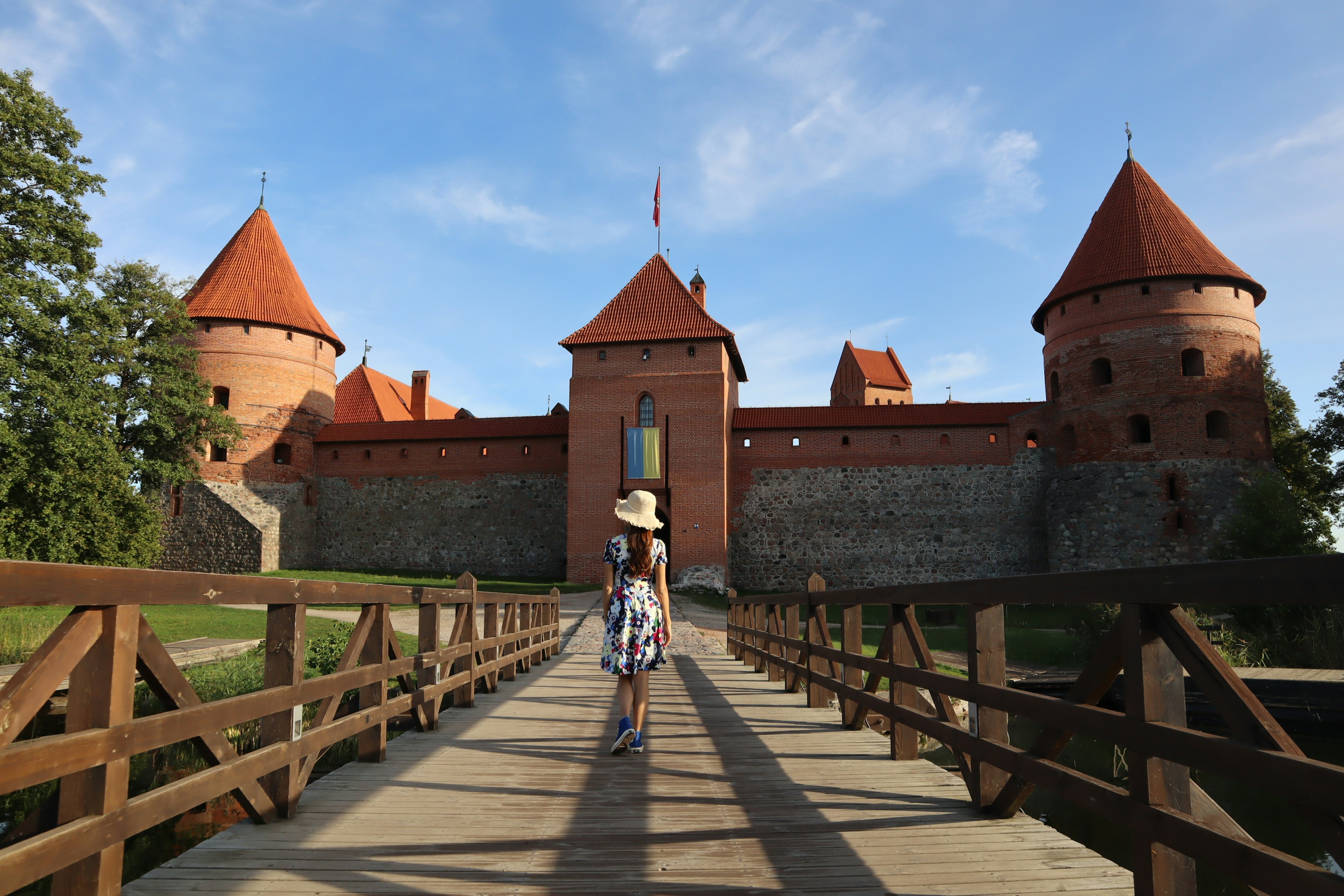 Woman walking on wooden bridge towards medieval castle with red roofs