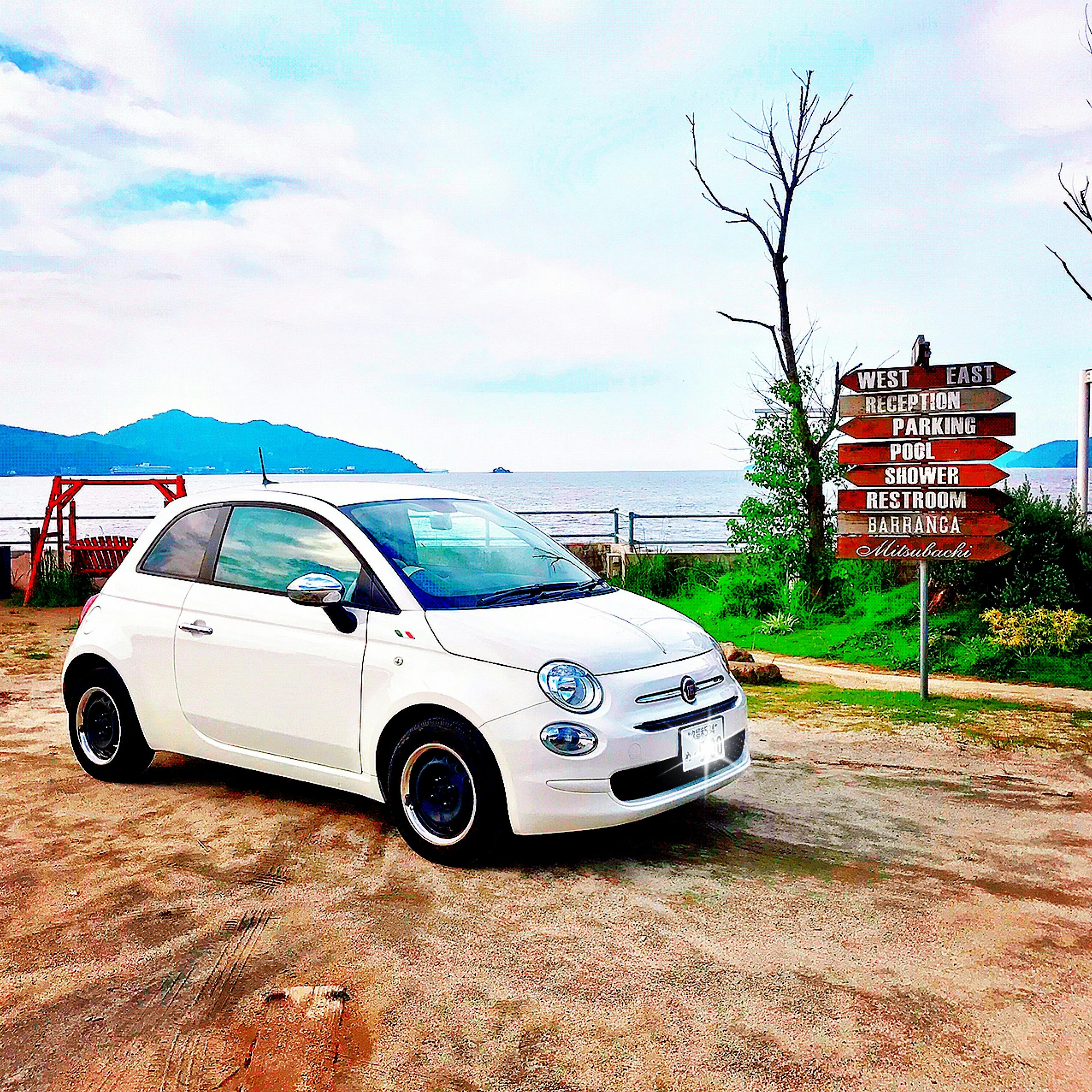 Fiat 500 สีขาวจอดใกล้ทะเลพร้อมป้ายทิศทาง