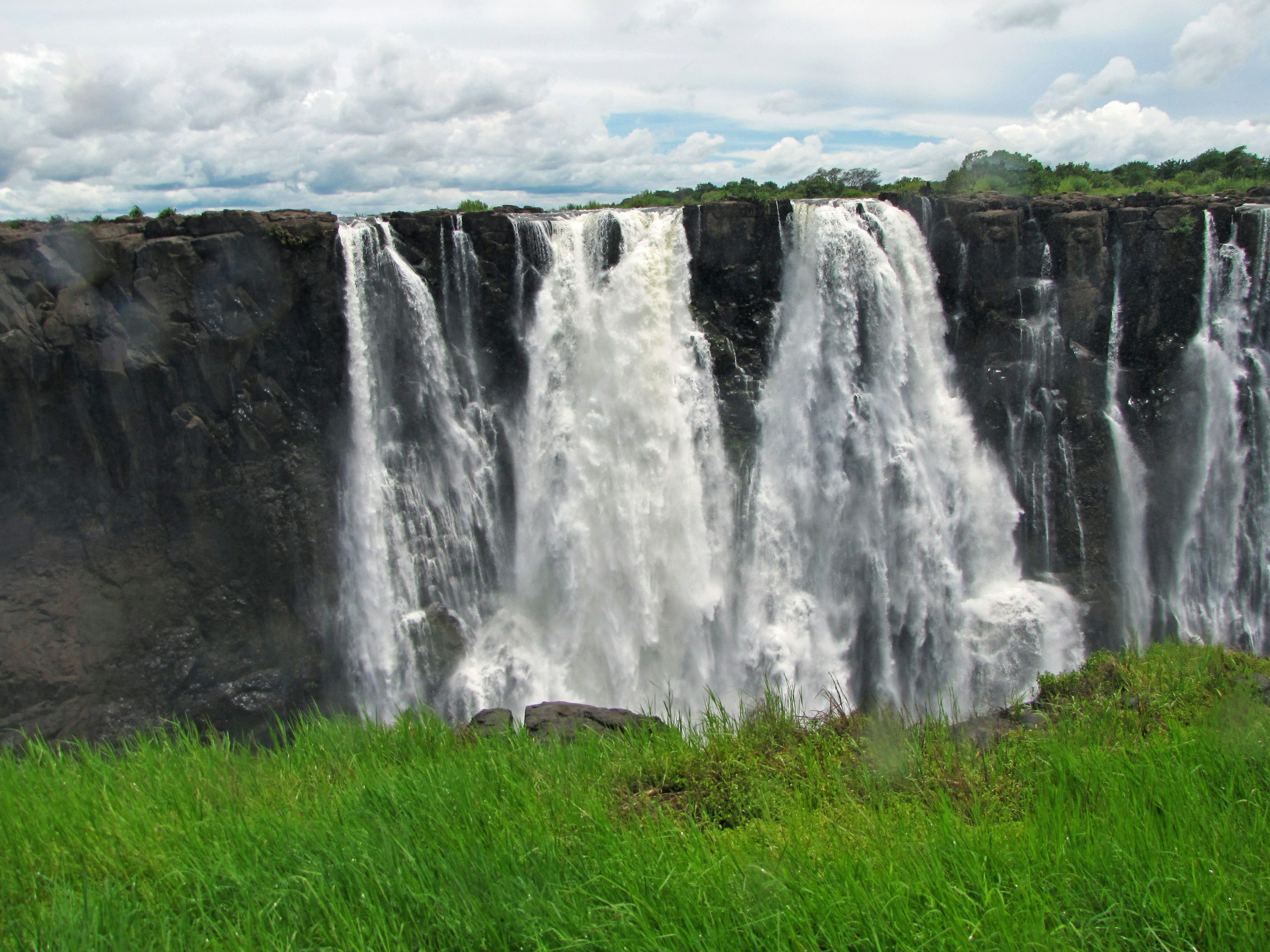 Un paesaggio con una cascata che scorre su una scogliera rocciosa circondata da erba verde lussureggiante