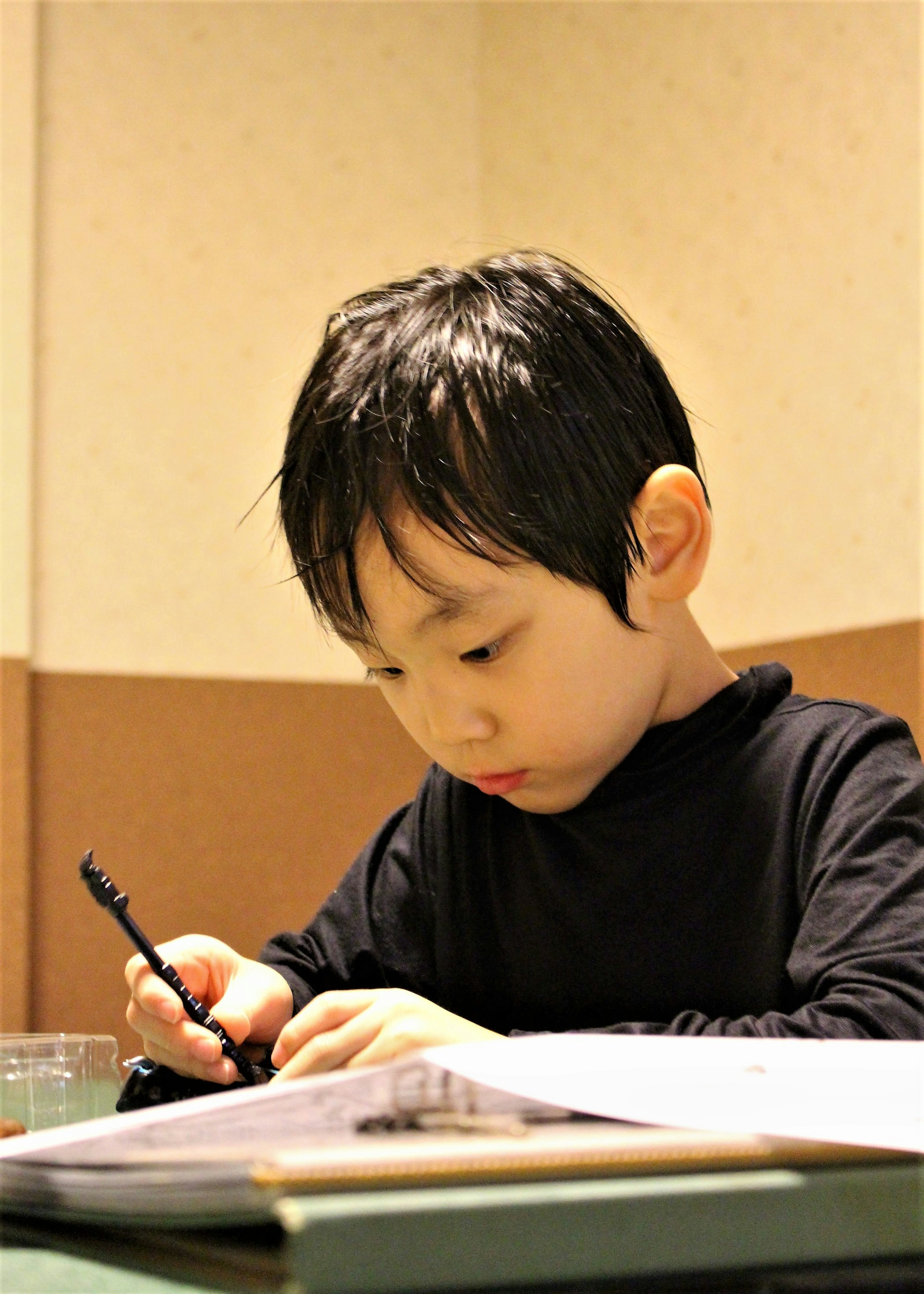 Enfant en chemise noire concentré sur l'écriture