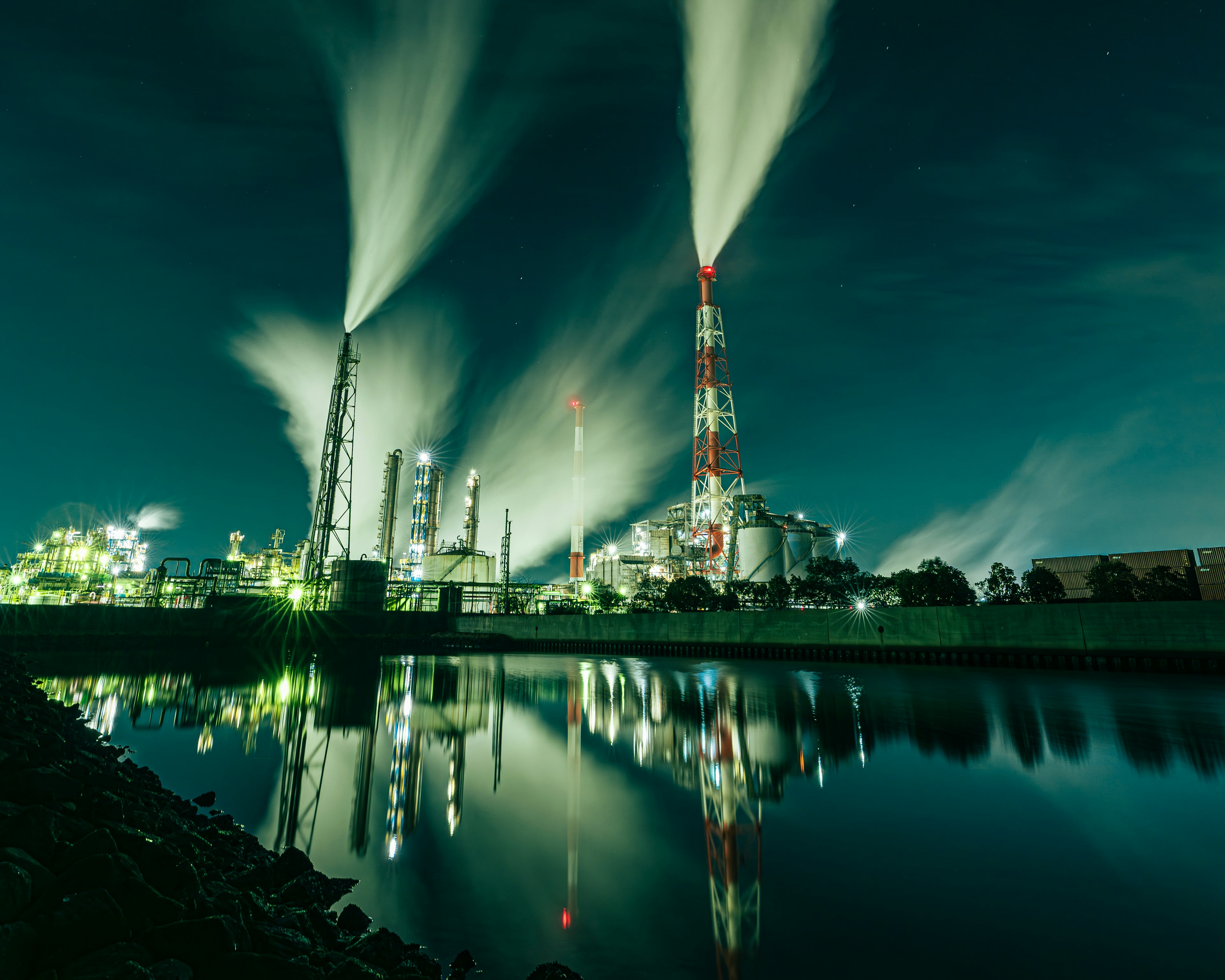 Night industrial scene with smokestacks emitting vapor and reflections on the water