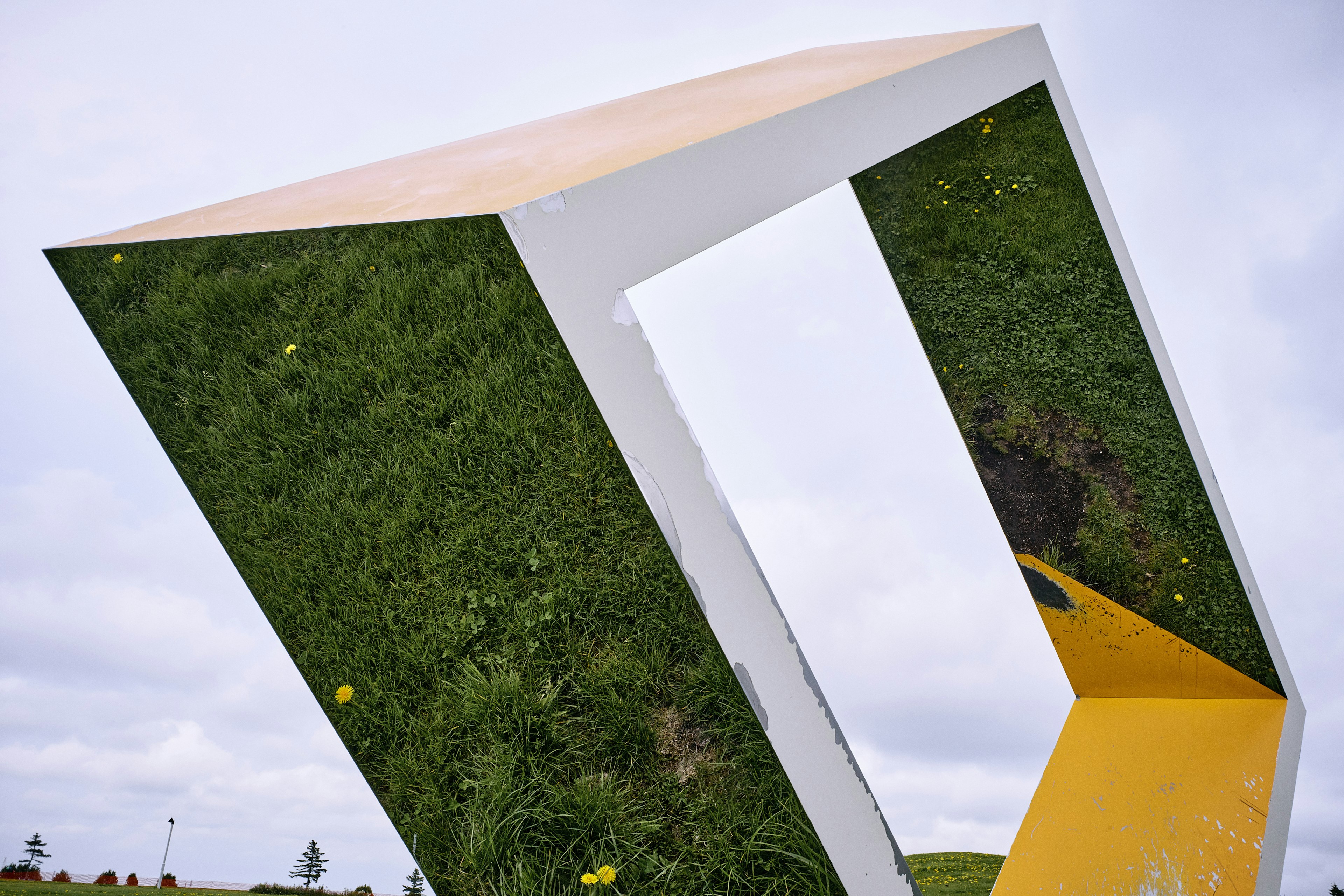 Una escultura geométrica que refleja hierba verde y flores amarillas