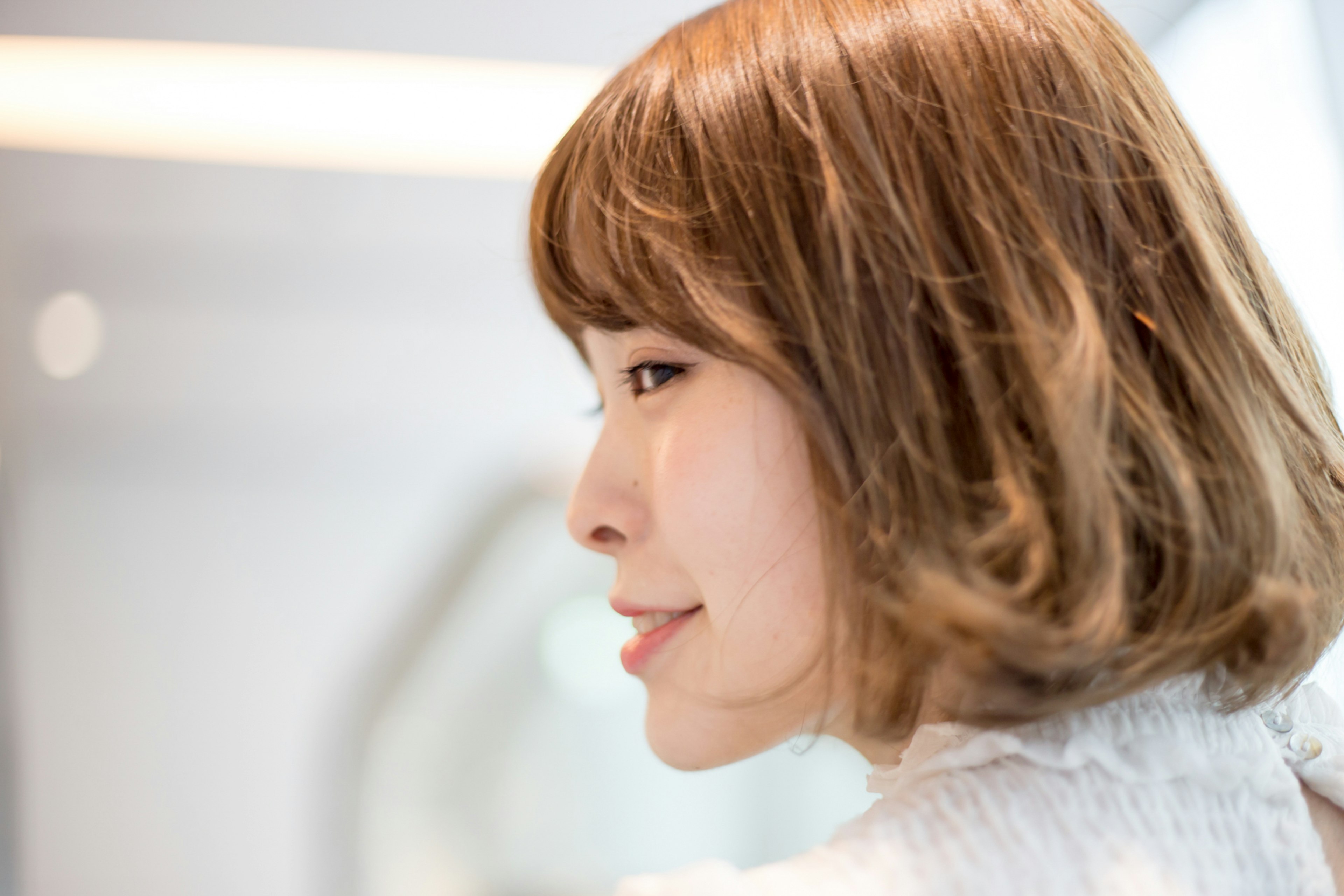 Une femme souriante de profil avec des cheveux bruns à la longueur des épaules dans un fond lumineux