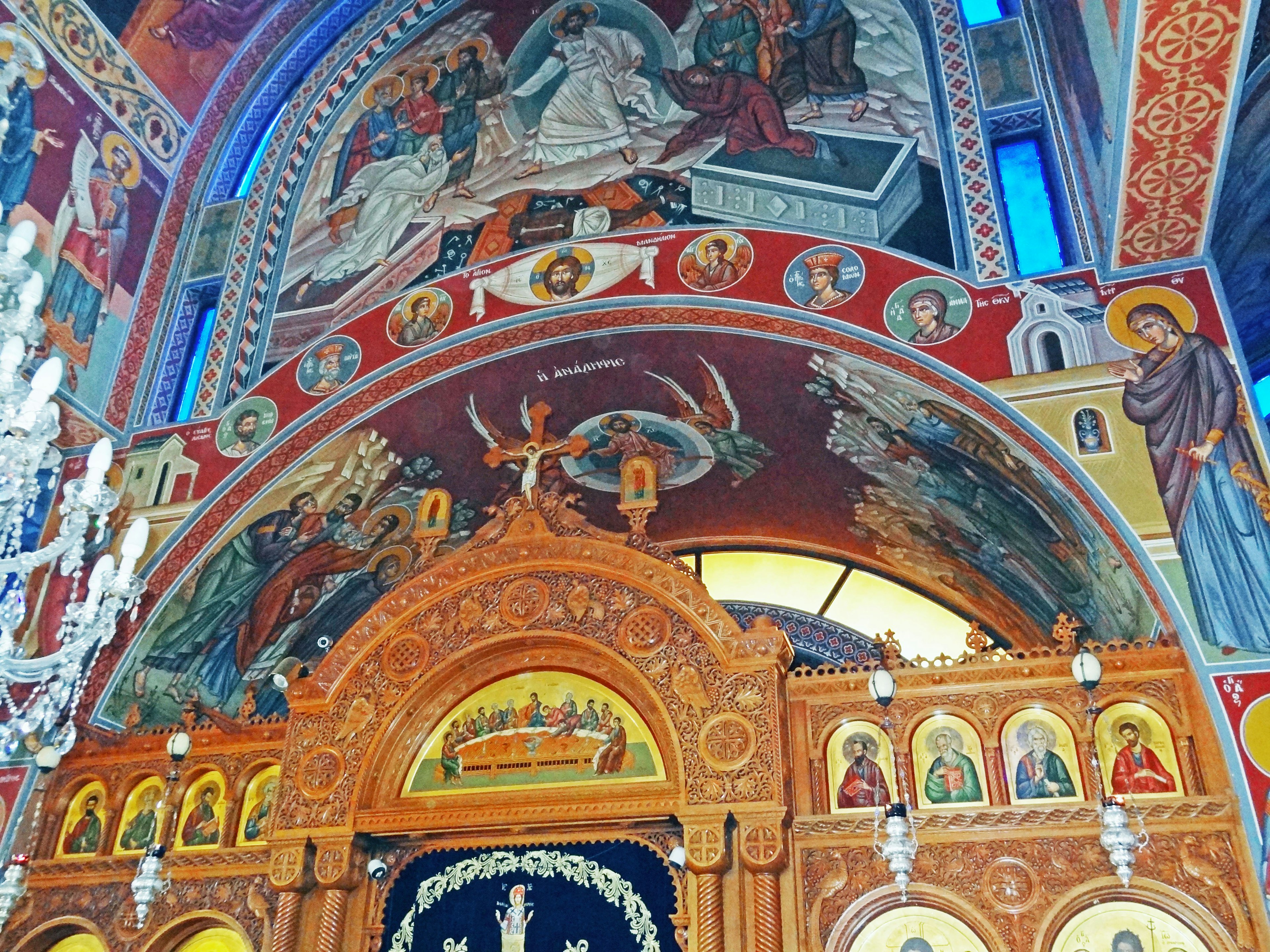 Interior of a church featuring vibrant religious murals and ornate chandeliers