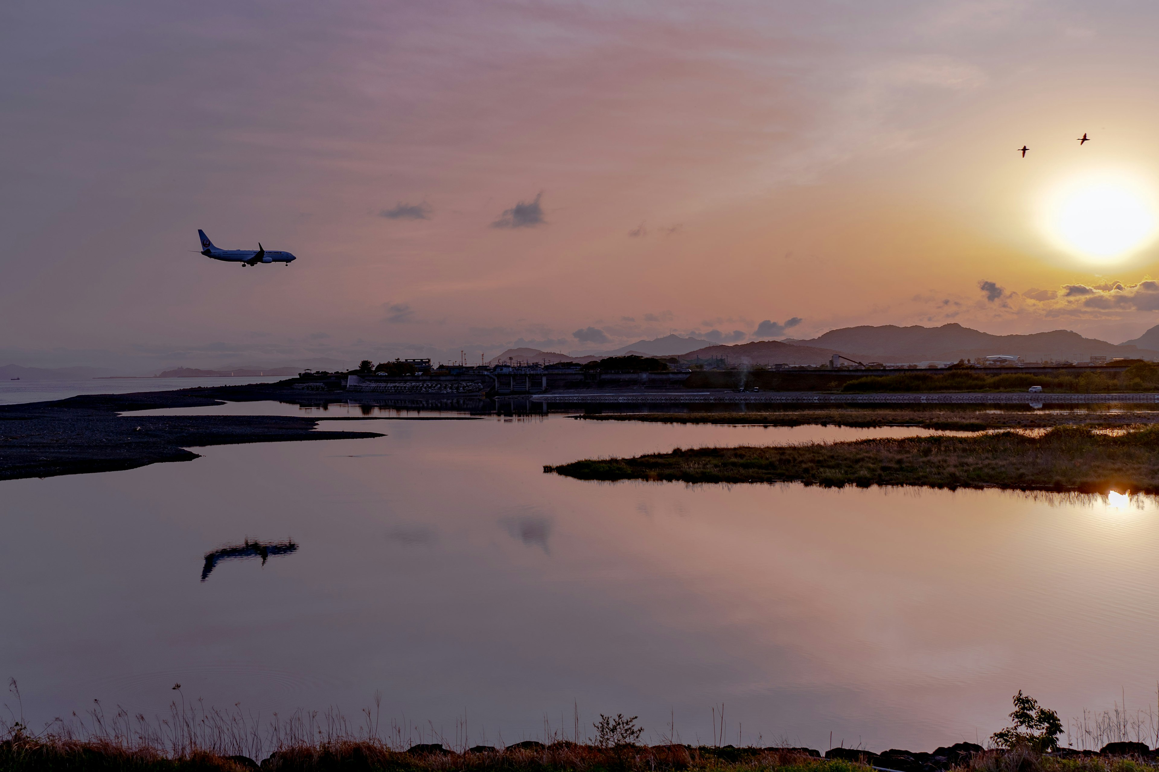 Airplane flying during sunset with reflection on calm water