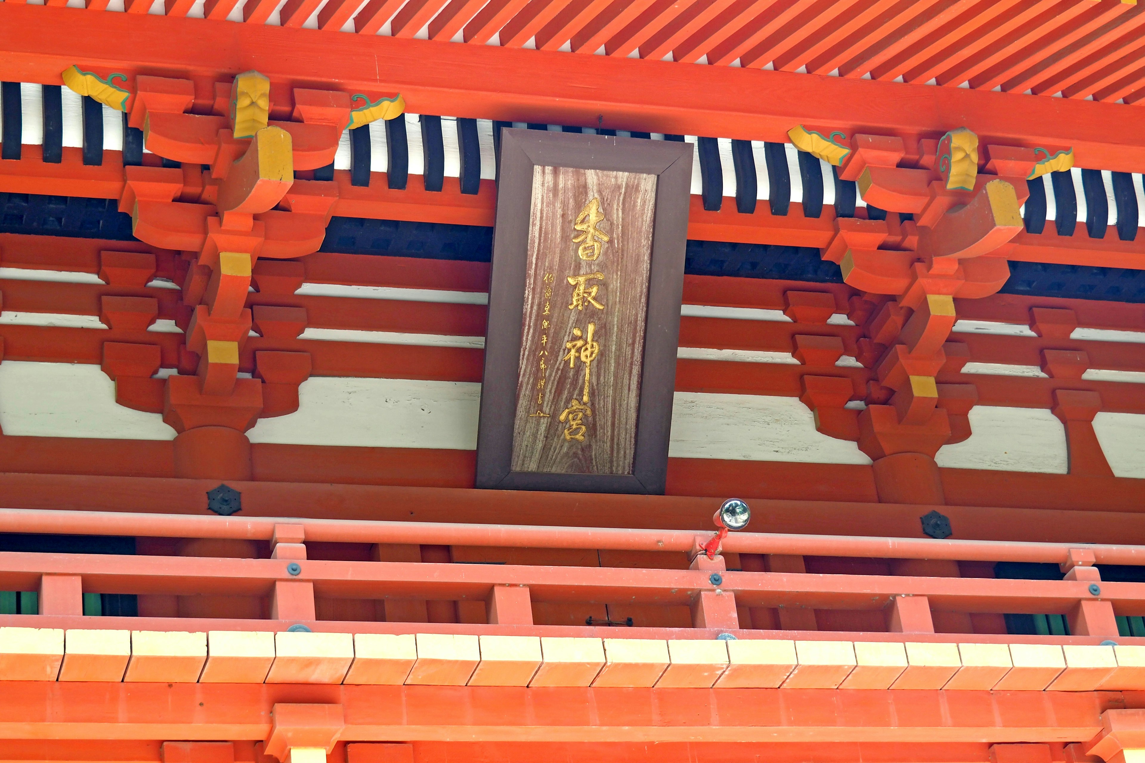 Vibrant red shrine architectural detail featuring a wooden sign overhead