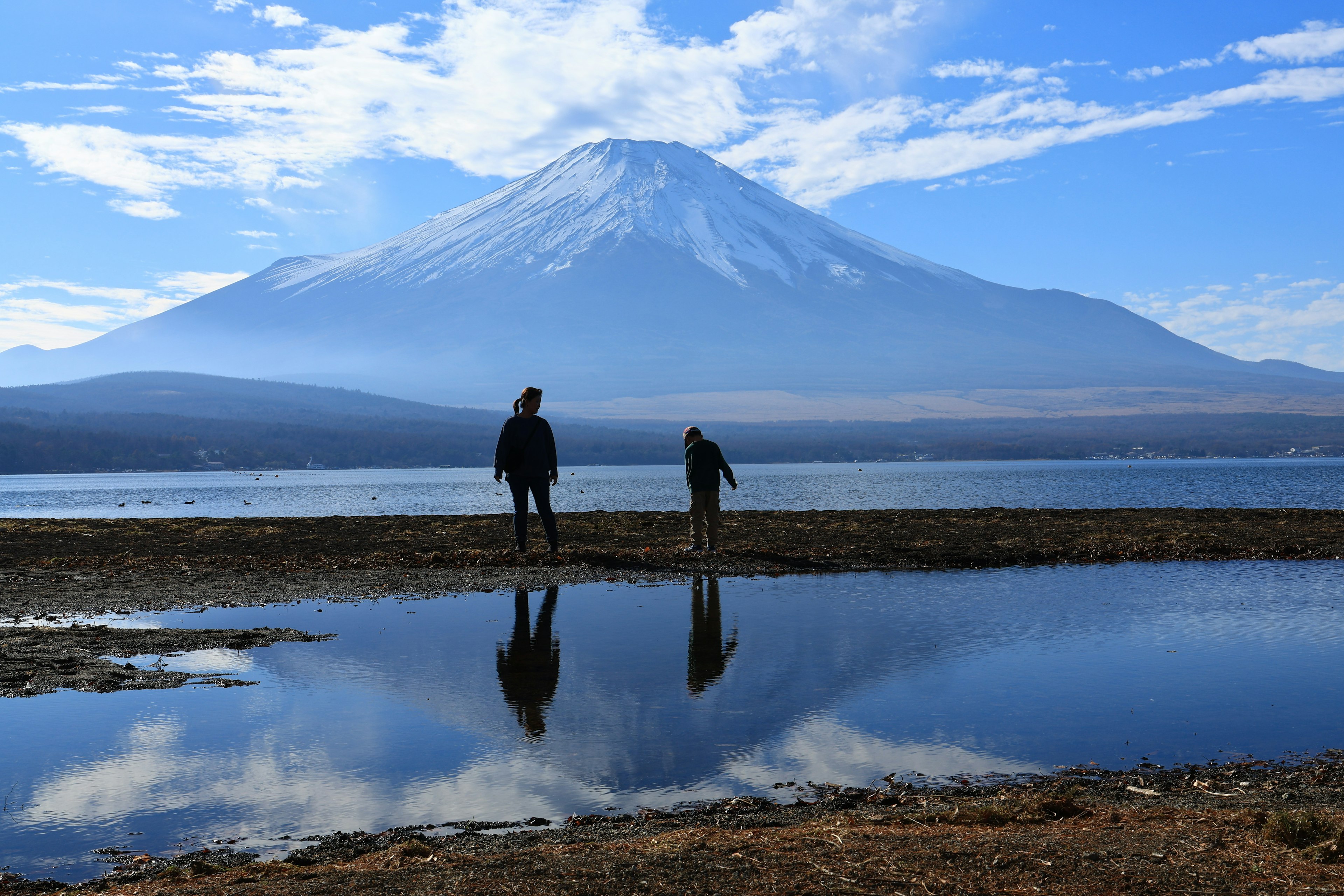 富士山を背景にした湖のほとりに立つ二人の人影