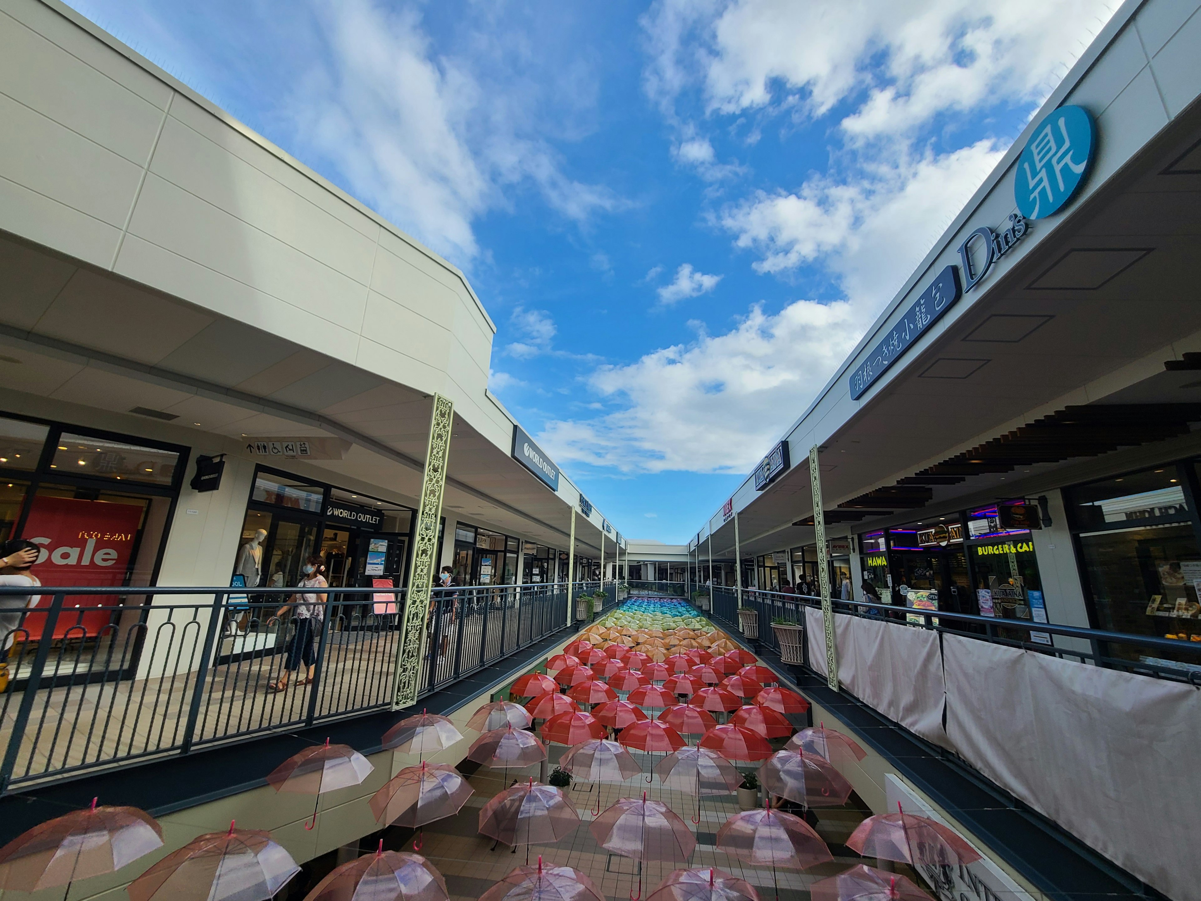 Shopping mall walkway under blue sky featuring red umbrella art installation