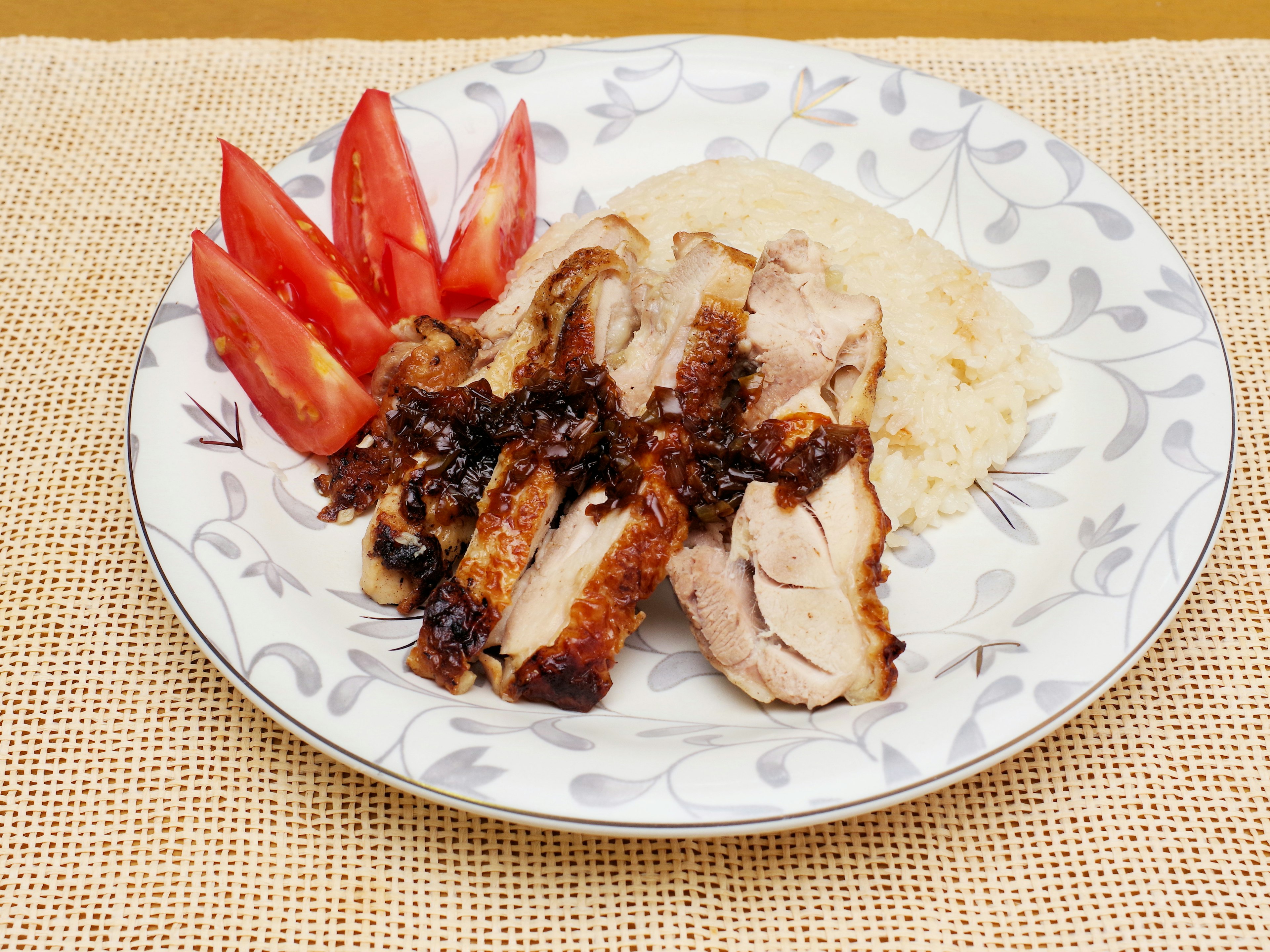 Dish of sliced chicken served with rice and tomato wedges on a decorative plate