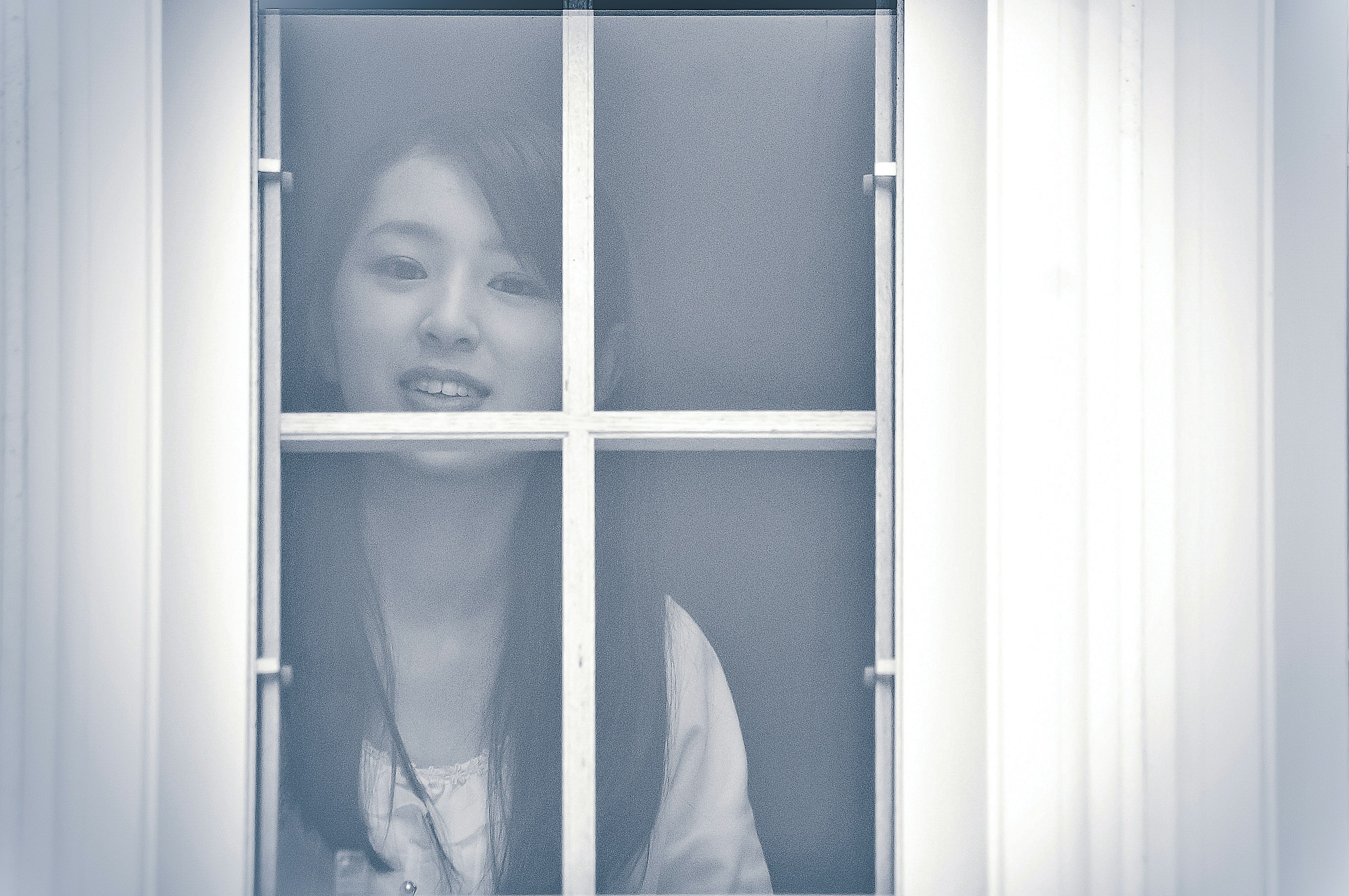 A woman smiling seen through a window in a soft blue tone