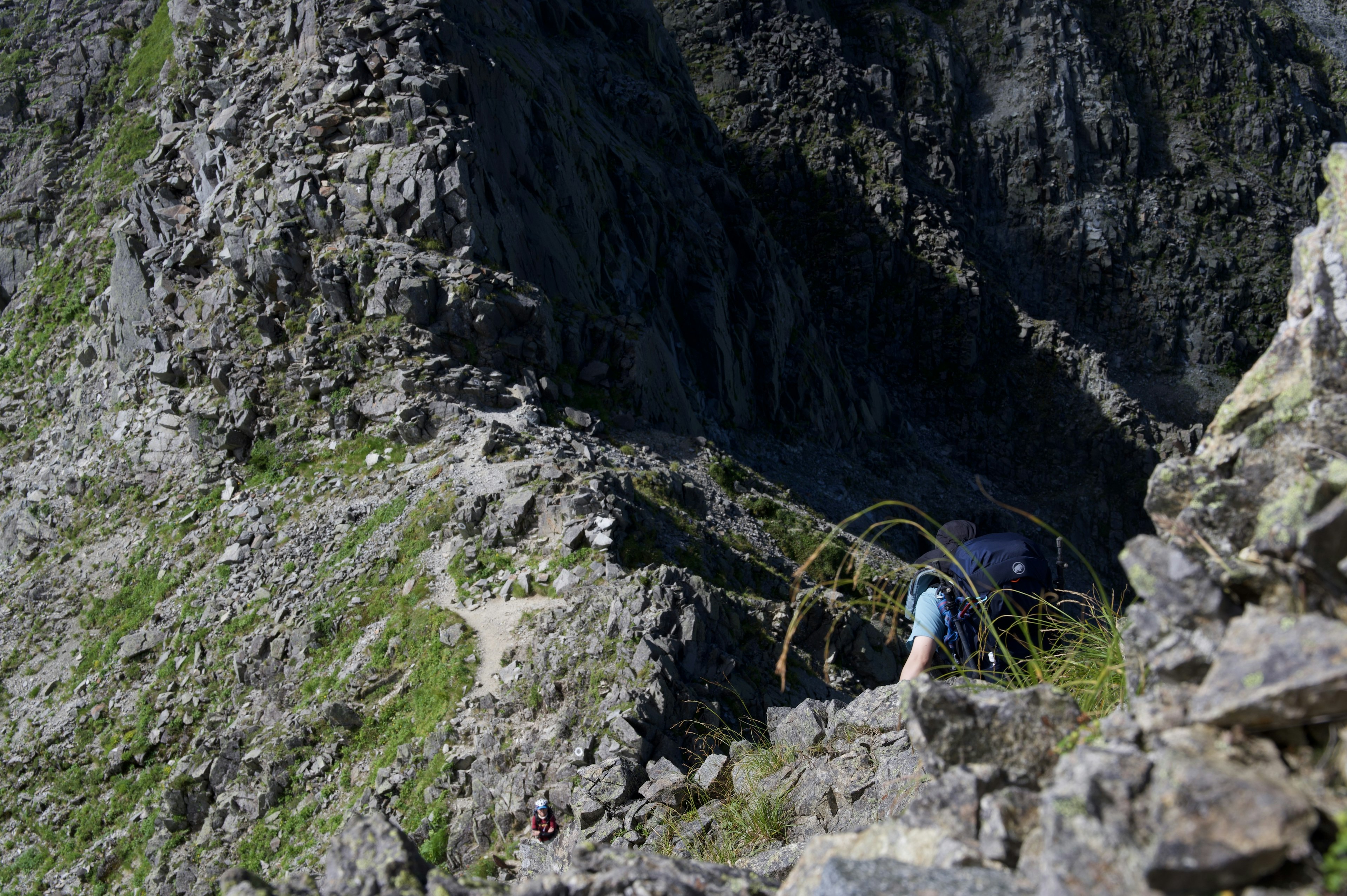 Hiker climbing a rocky cliff with visible green grass and rock textures