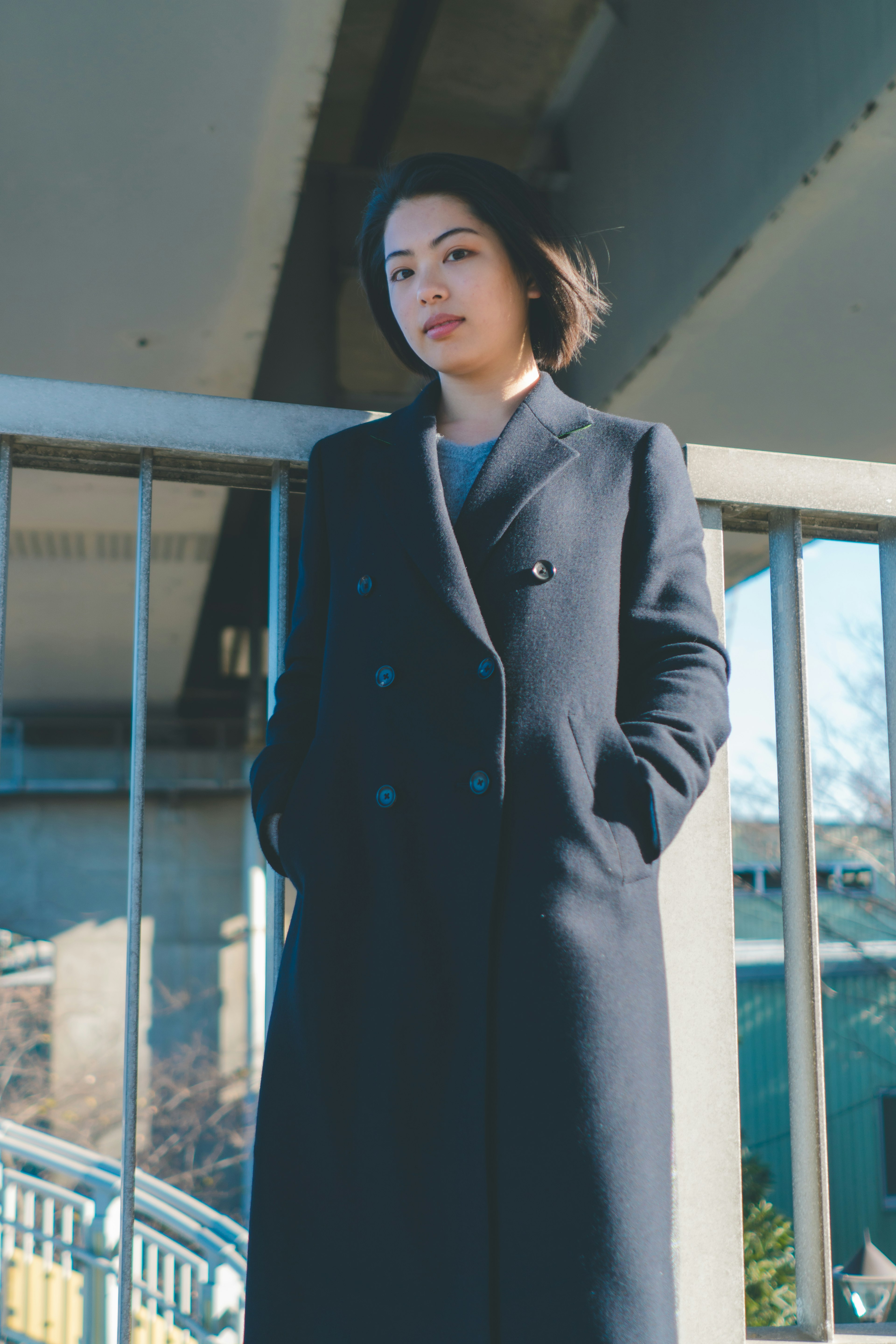 A woman stands under a bridge wearing a dark coat