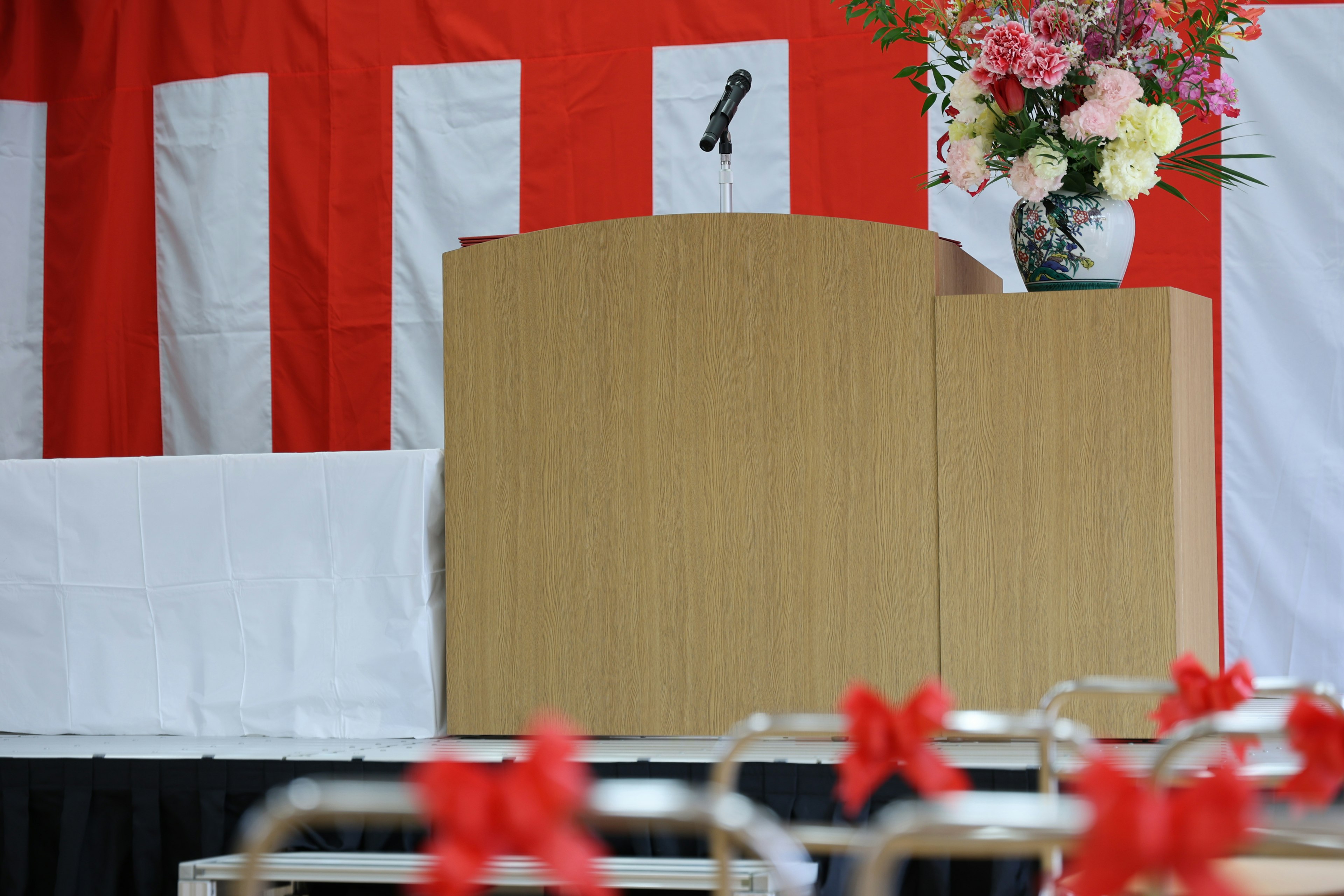 Podium mit Mikrofon und Blumenarrangement vor rotem Hintergrund