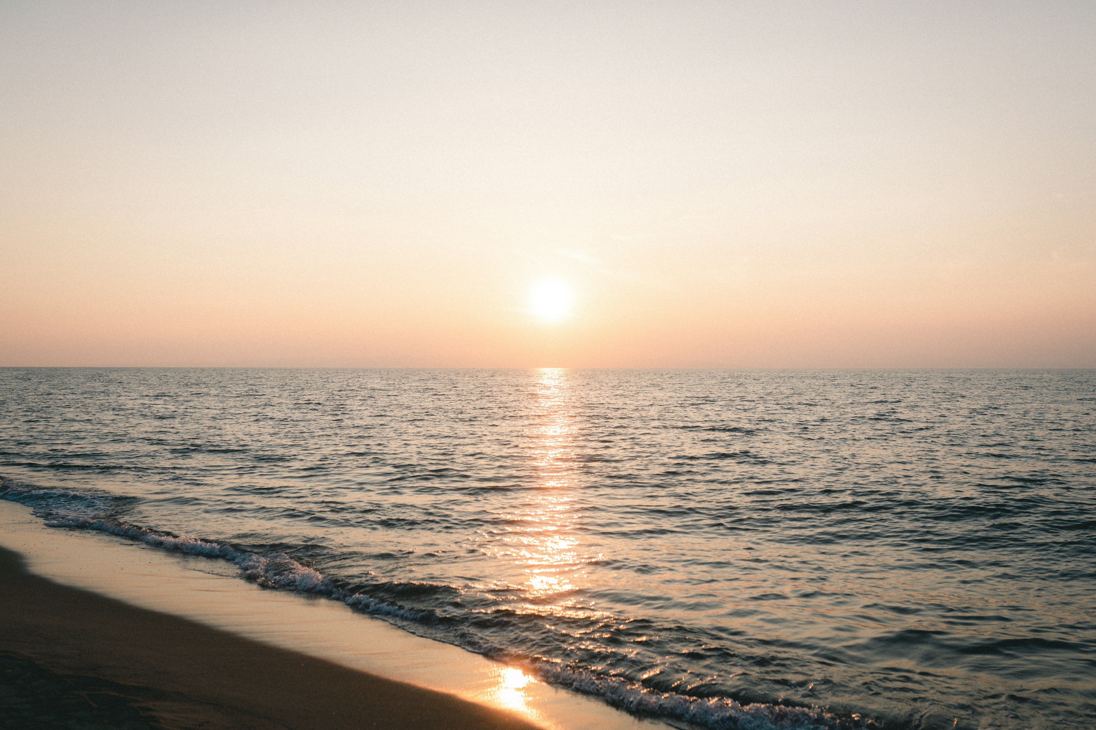 Ruhige Strandansicht mit Sonnenuntergang, der sich auf dem ruhigen Ozean spiegelt