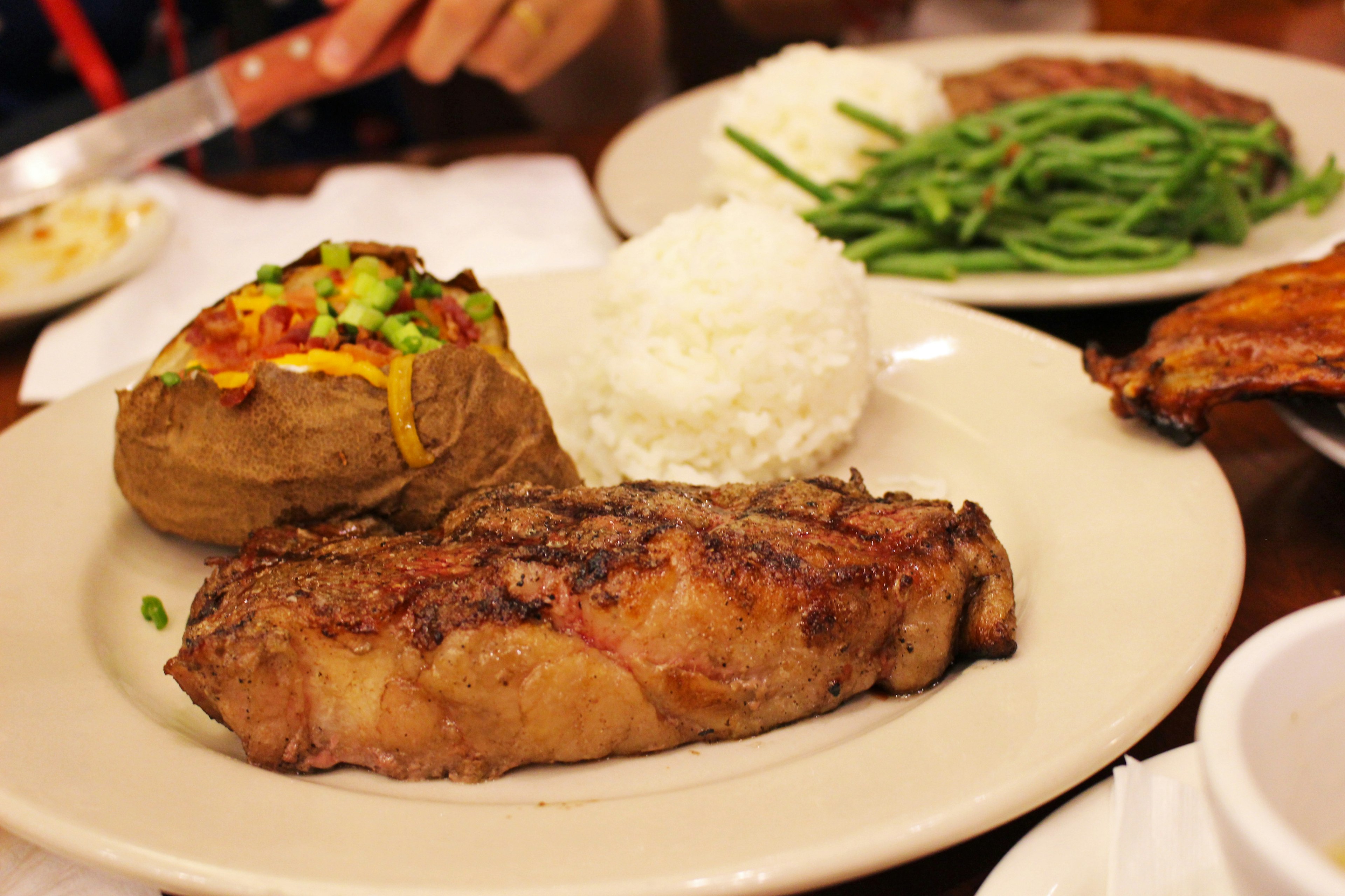 Steak tebal dengan kentang panggang berisi nasi putih dan kacang hijau di piring