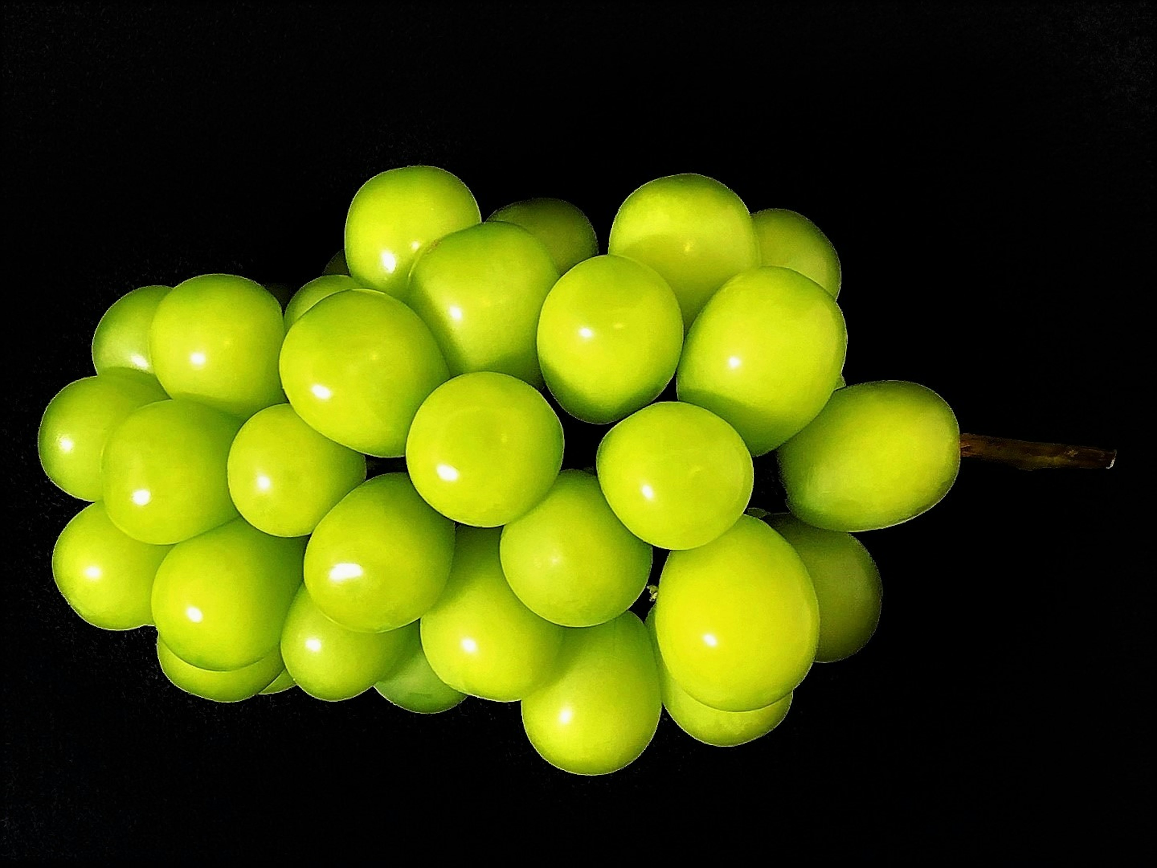 Un racimo de uvas verdes vibrantes sobre un fondo negro