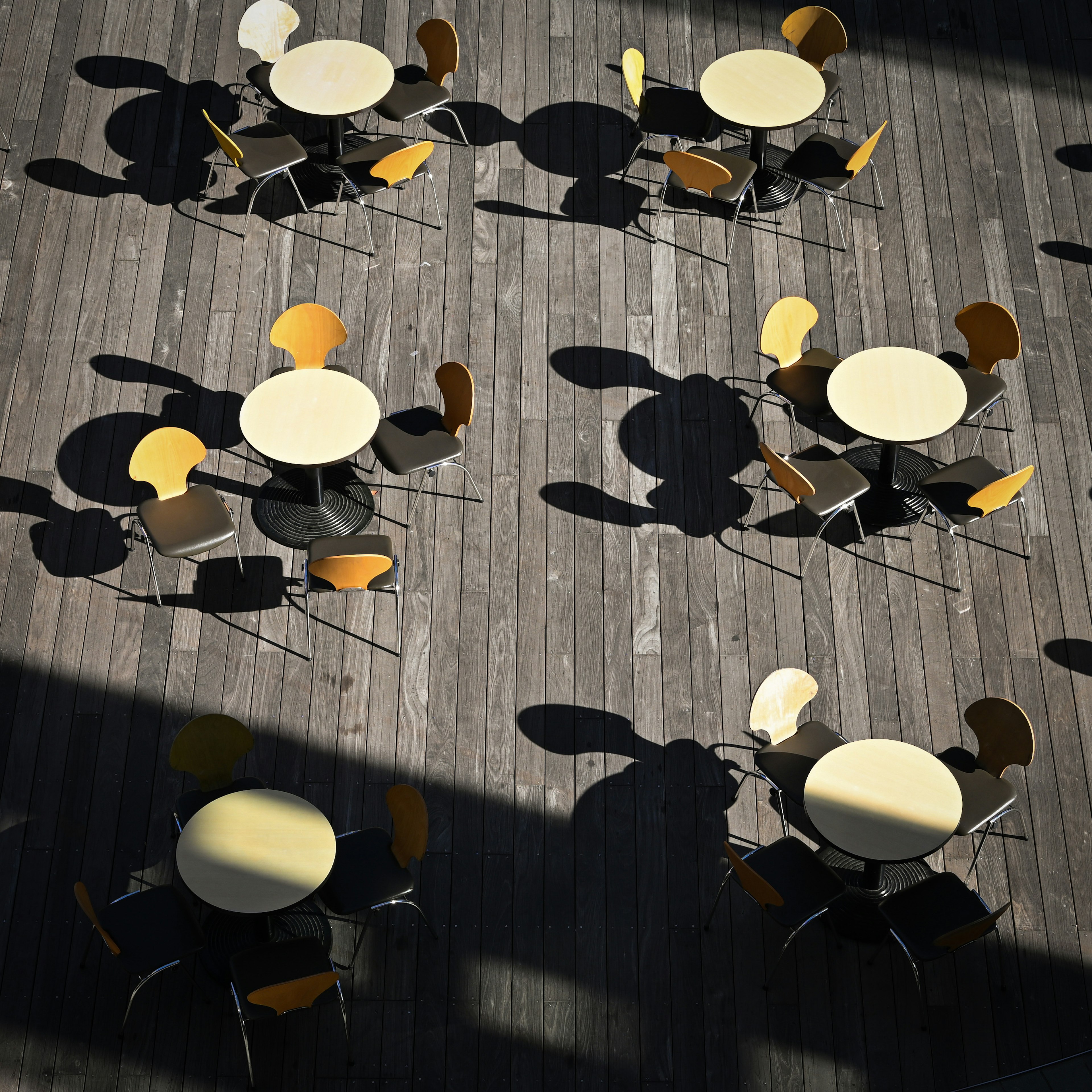 Circular tables with colorful chairs casting shadows on a wooden floor