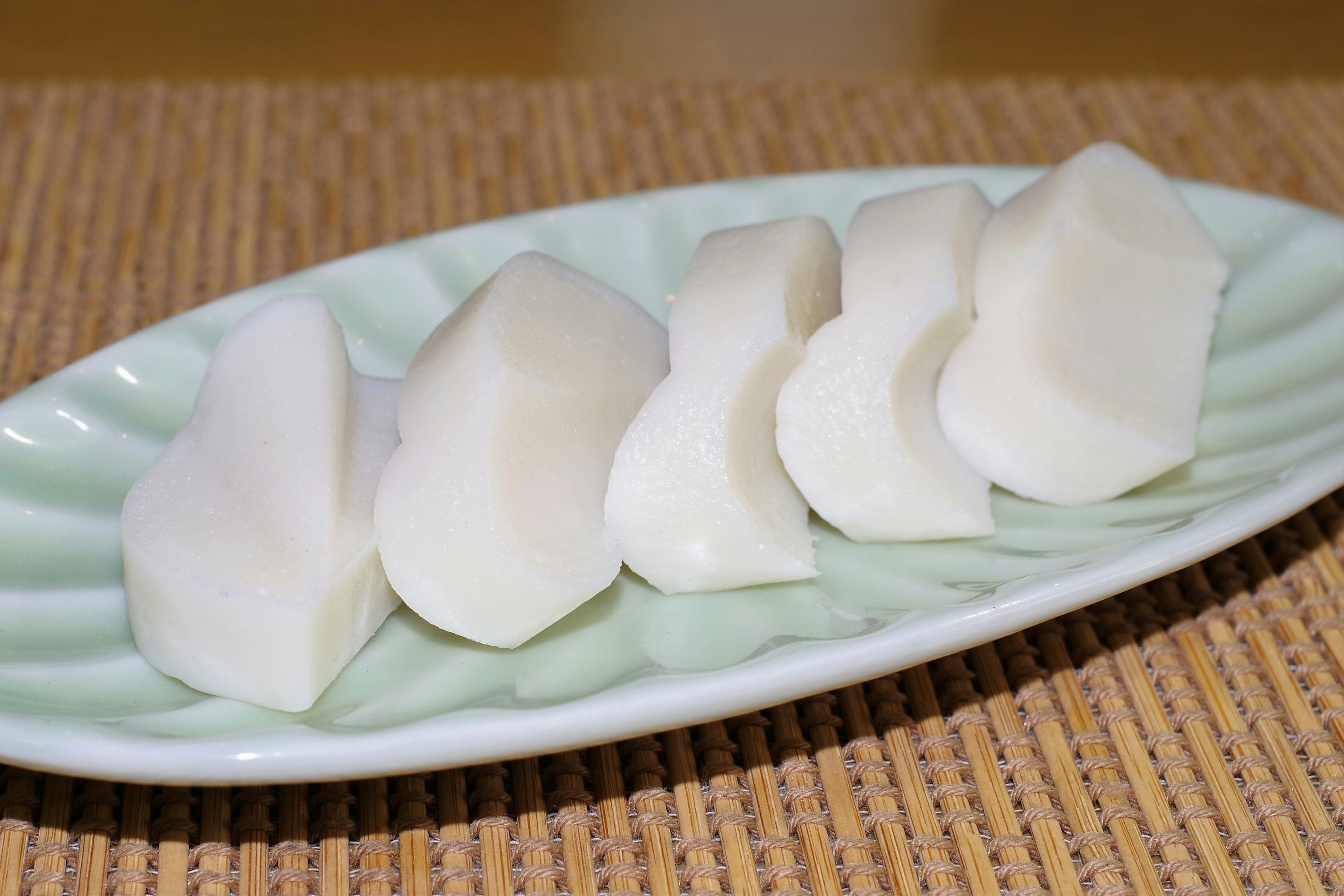 Sliced white daikon pickles arranged on a green plate