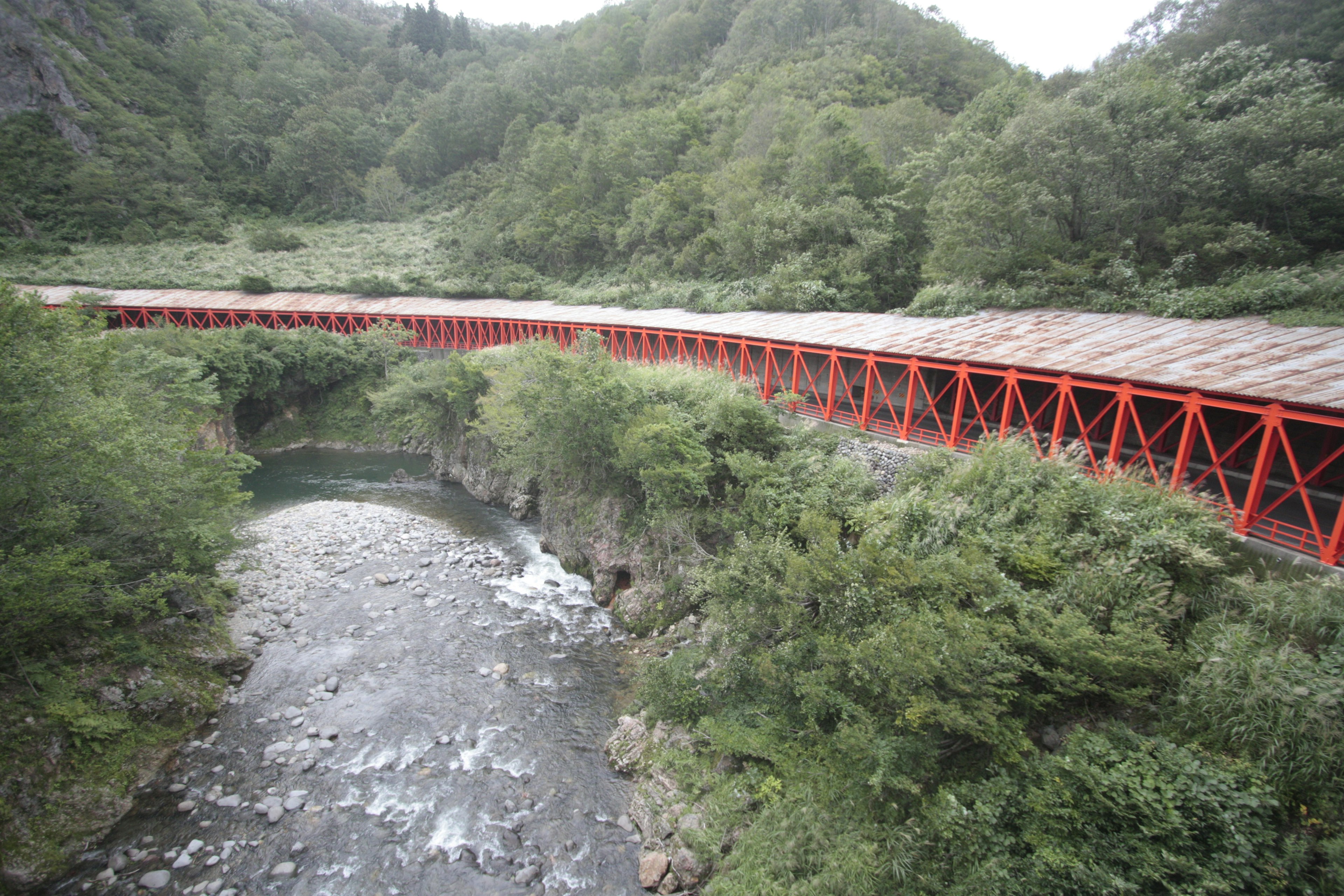 赤い鉄骨橋が緑の山々と川に架かる風景