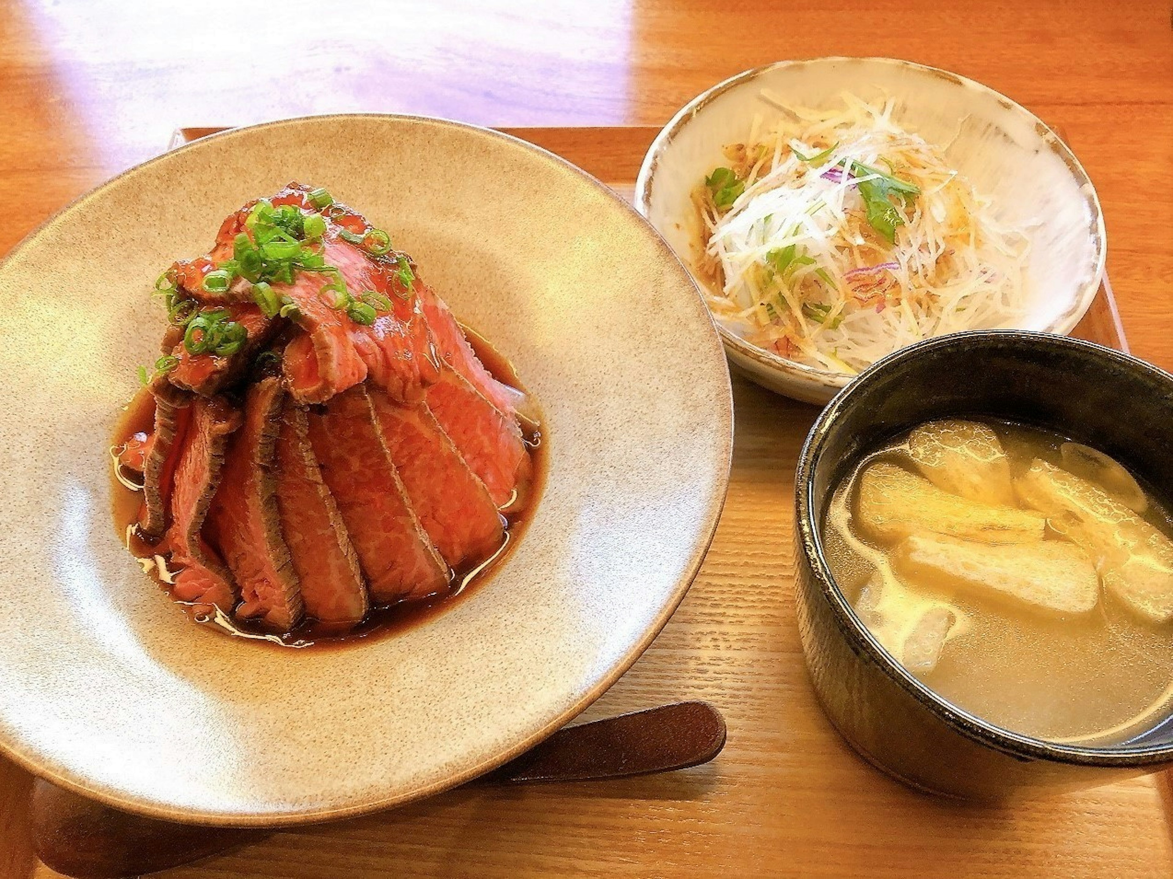 Plato de carne presentado deliciosamente con ensalada y sopa de miso