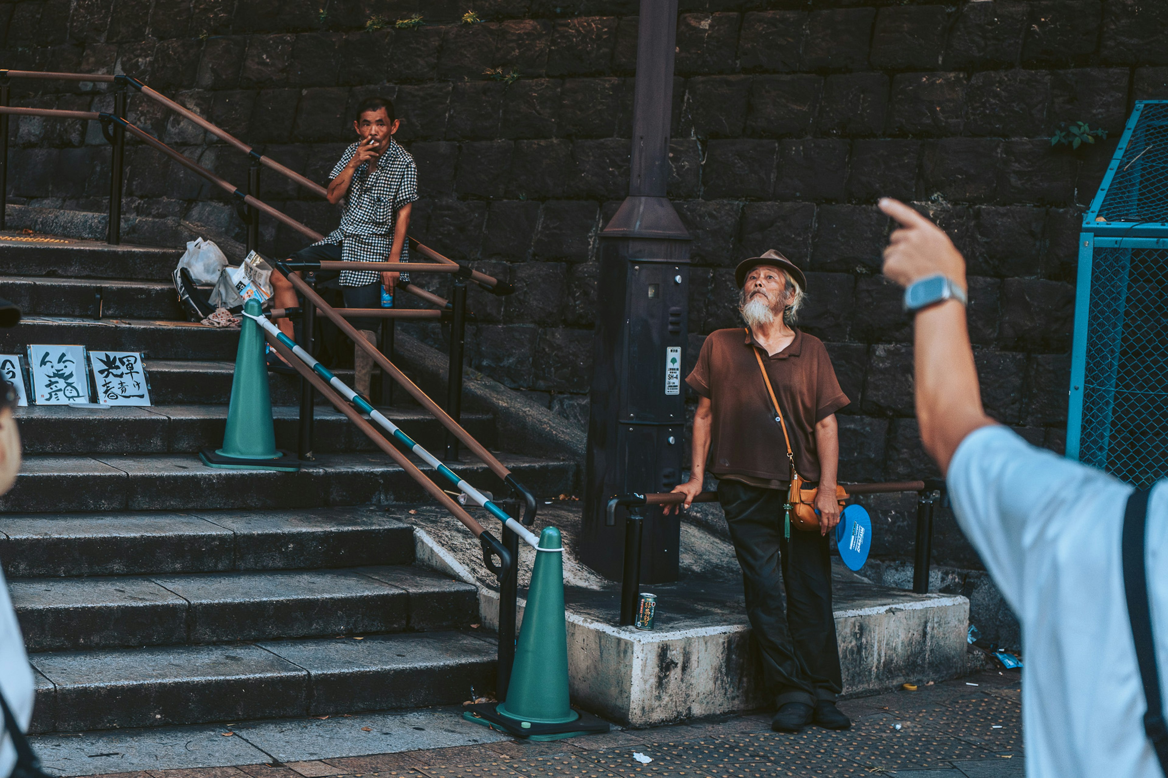 Street scene featuring a middle-aged man standing at the bottom of stairs and another man smoking