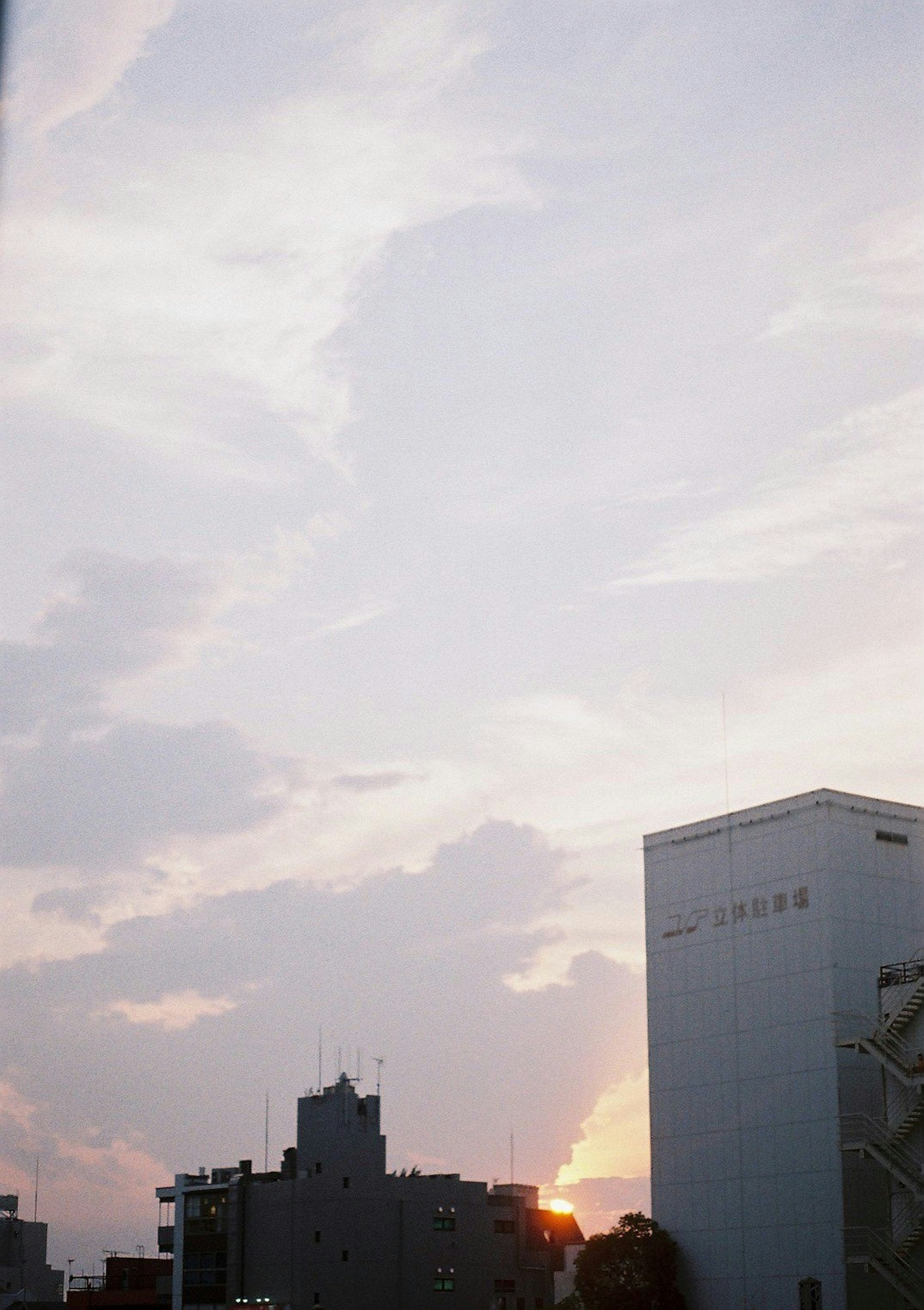 Cityscape at dusk featuring tall buildings and a sky with soft clouds