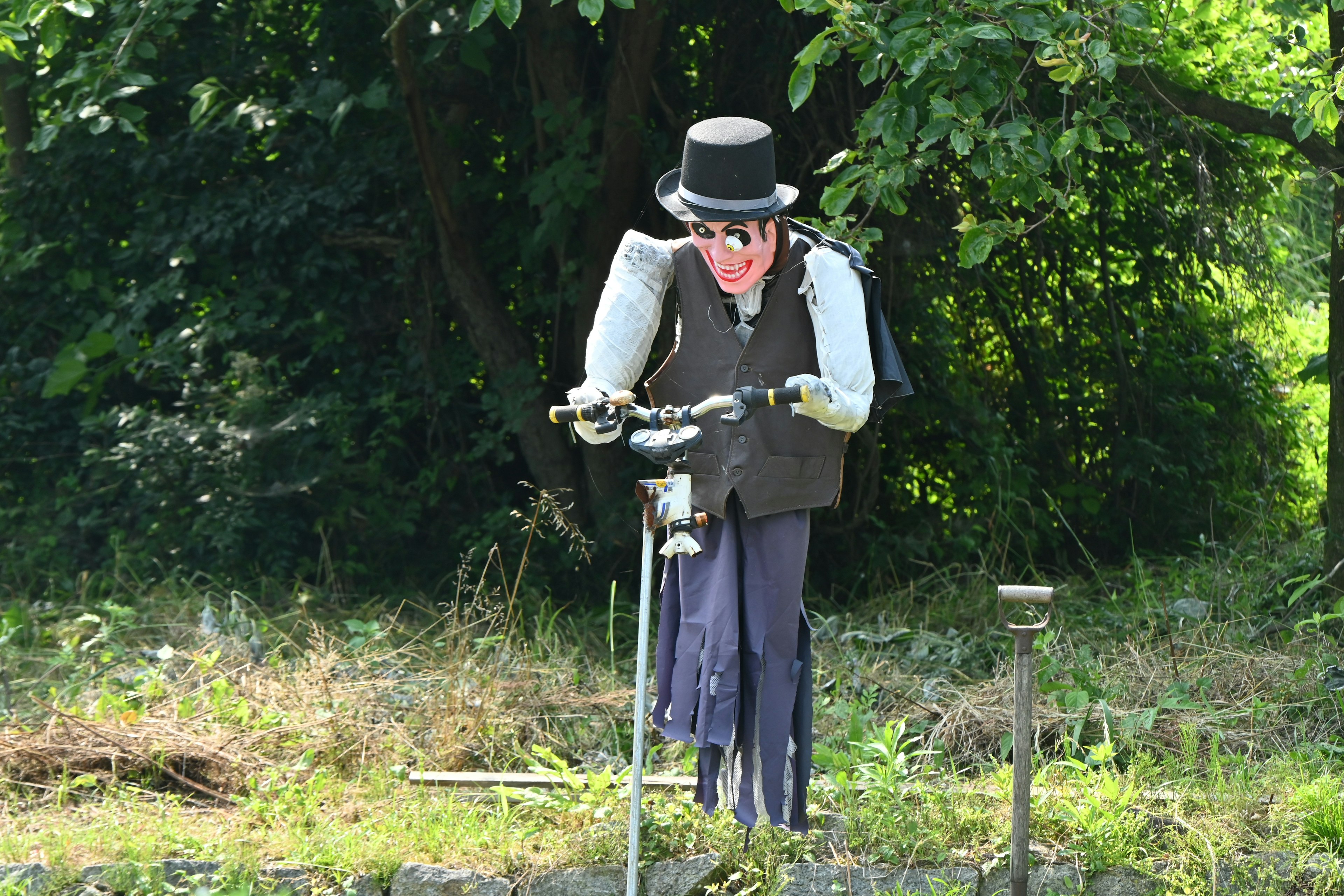 Un mannequin portant un chapeau tient des outils dans une zone herbeuse