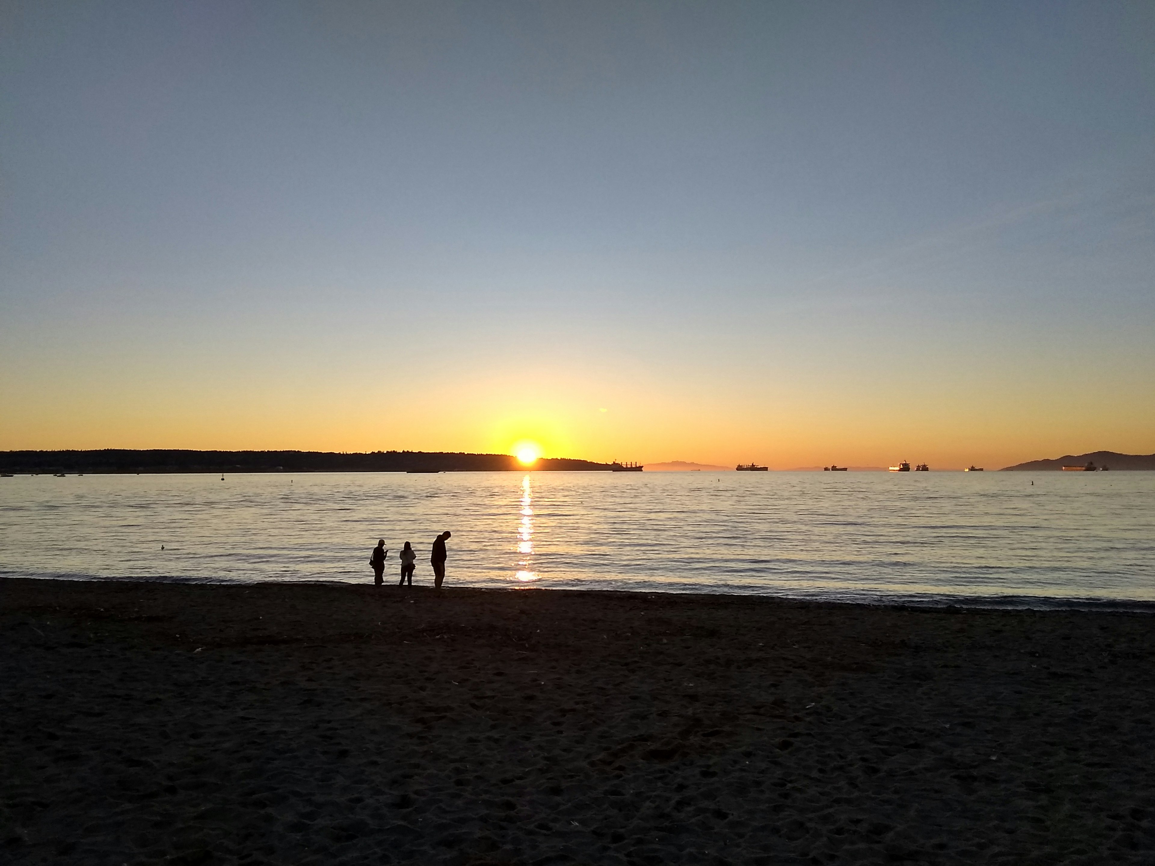 Des personnes debout sur une plage regardant le coucher de soleil sur l'océan