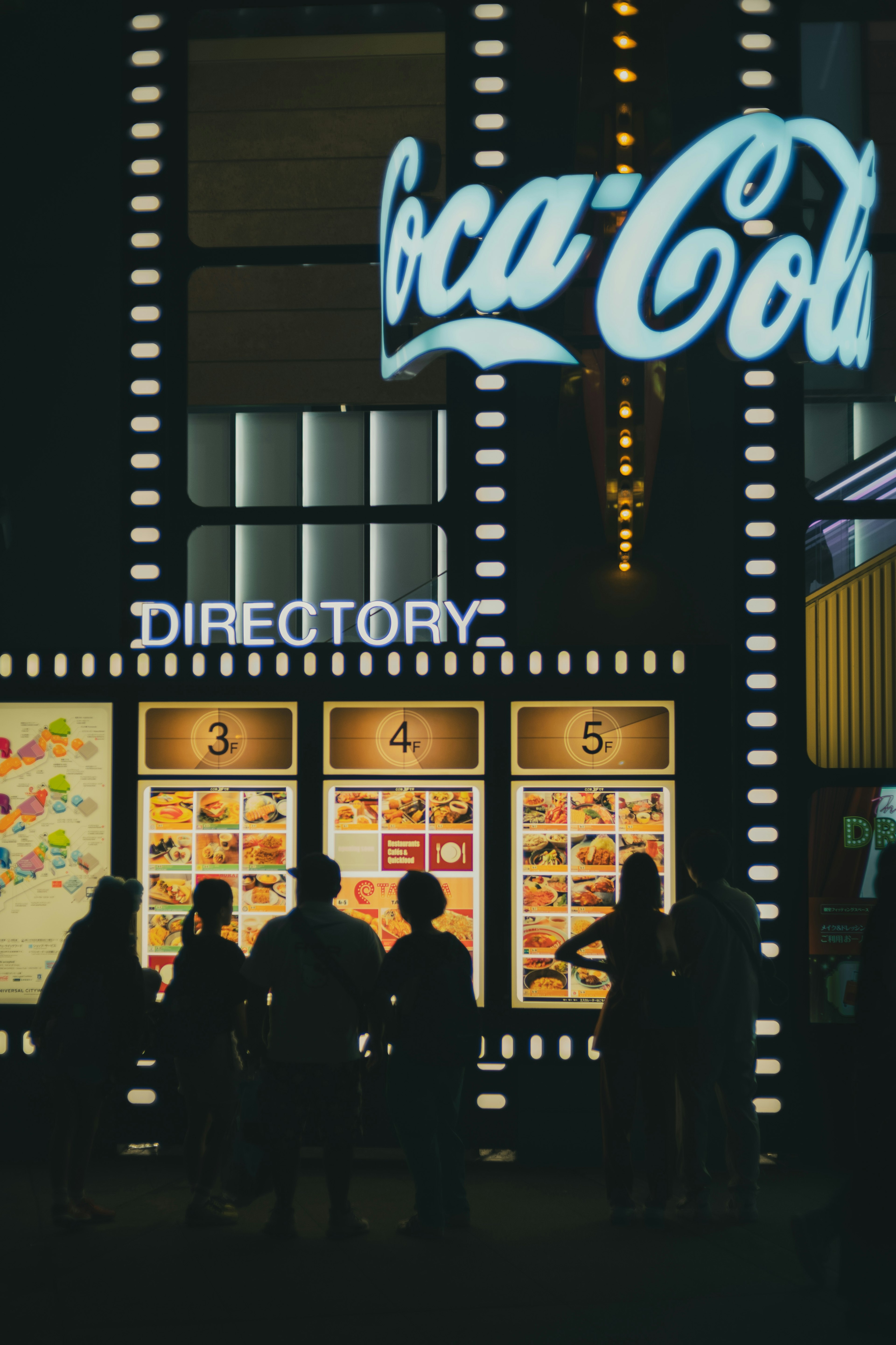 Silhouettes of people in front of Coca-Cola sign and directory