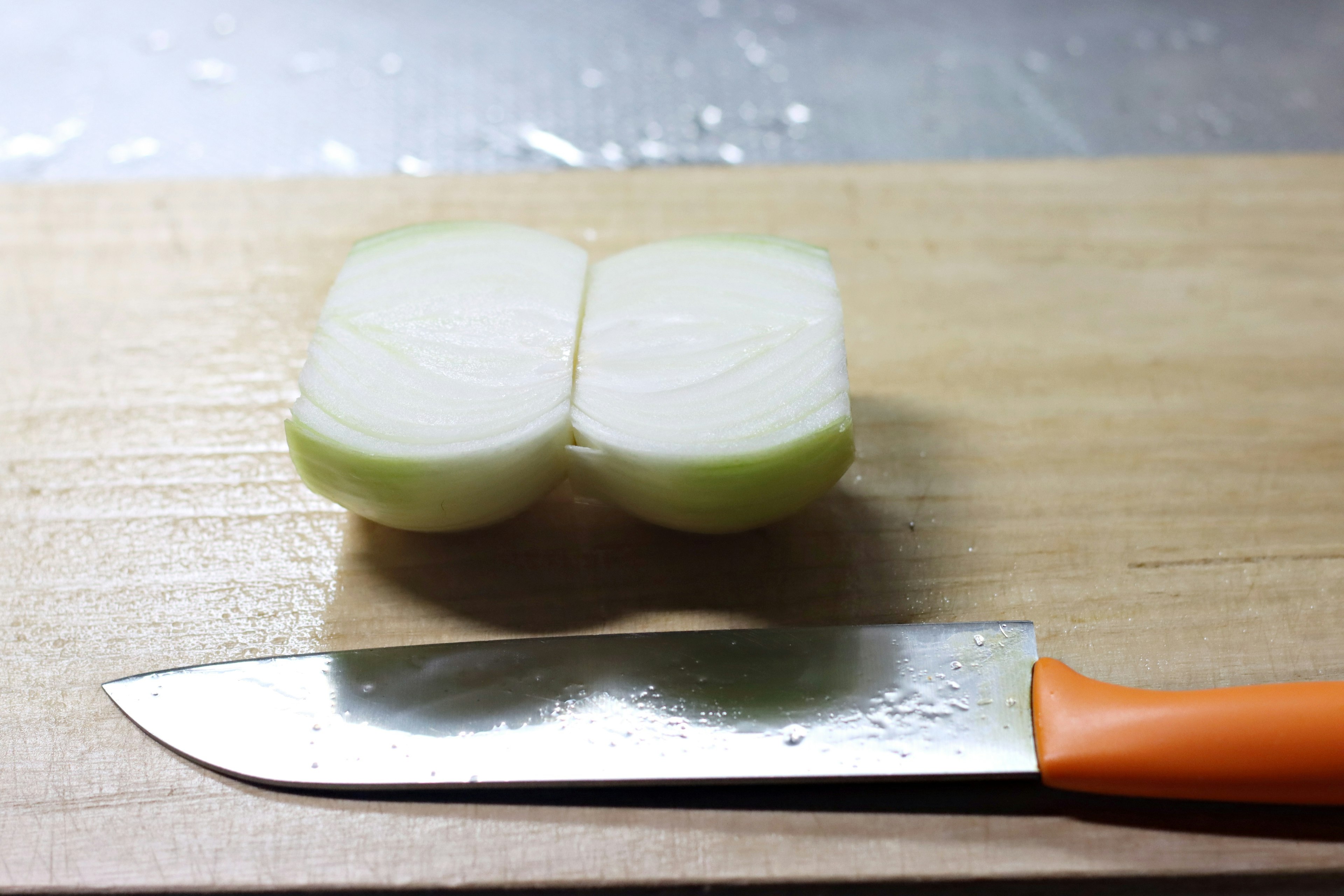 Halved onion with an orange kitchen knife on a wooden cutting board