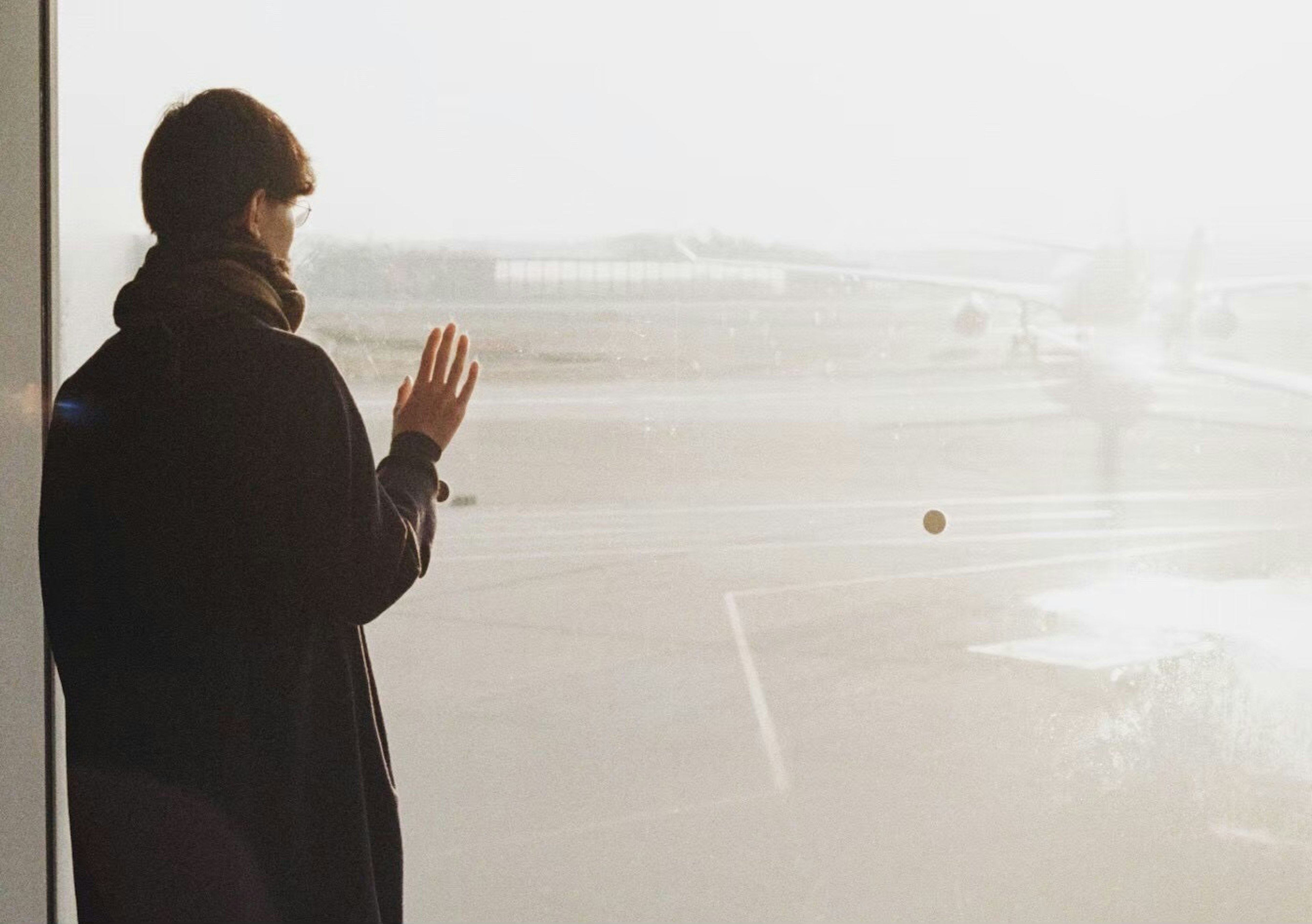 Person in a coat looking out the airport window waving goodbye