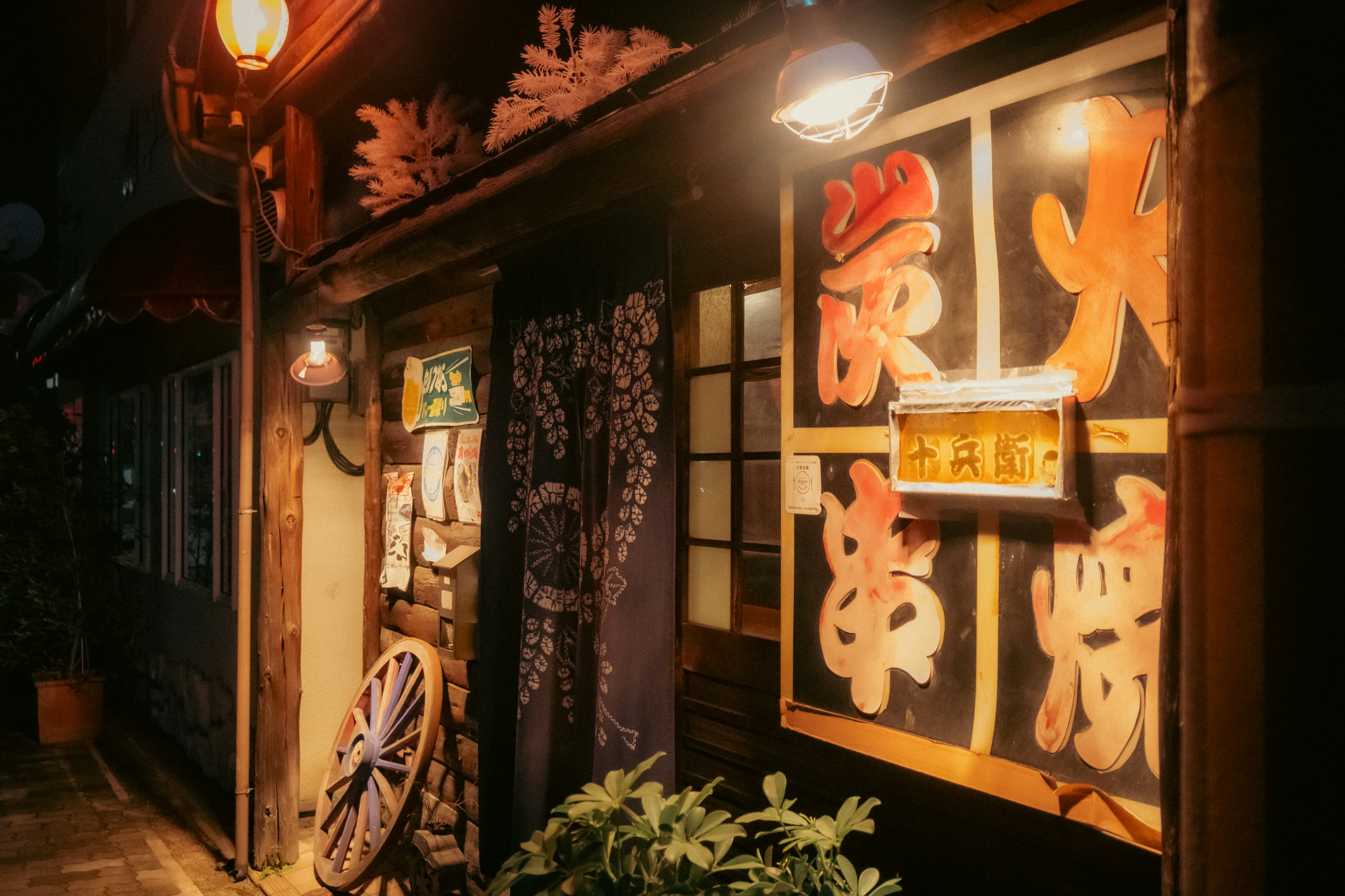 Exterior of a traditional Japanese izakaya at night featuring red lanterns and handwritten signs