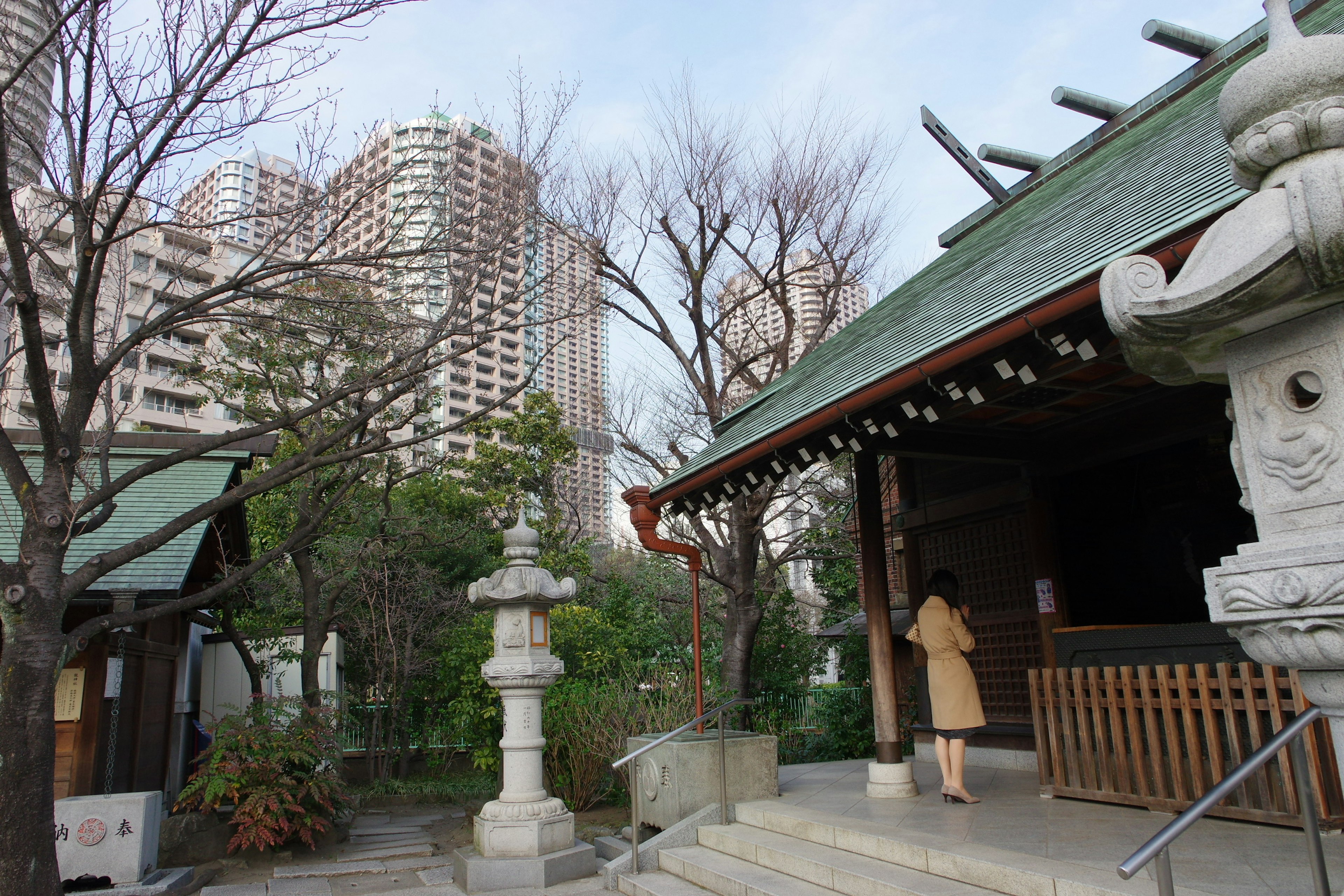 Urban shrine with high-rise buildings in the background a woman walking towards the shrine