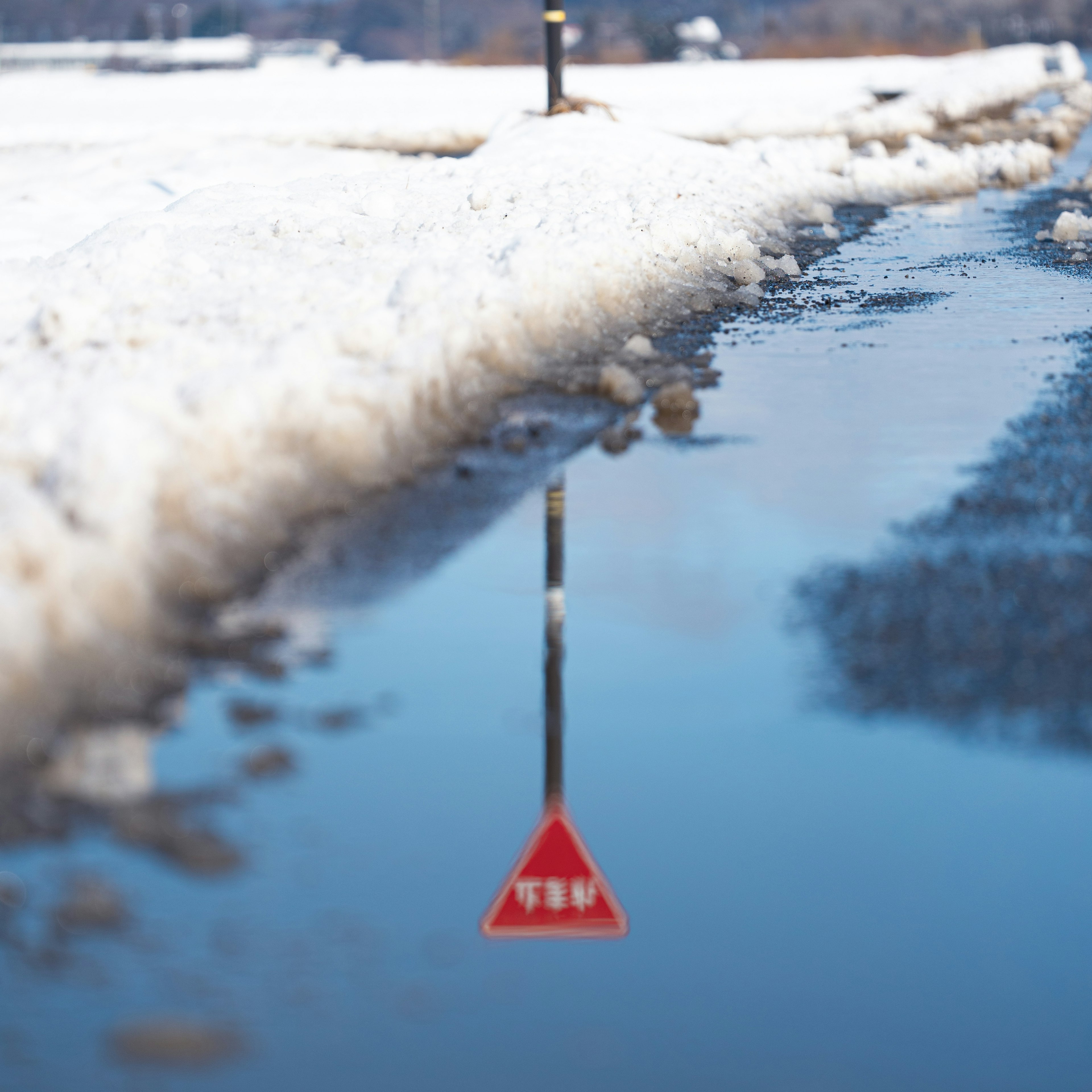 Reflexion eines roten dreieckigen Warnschildes in einer Pfütze umgeben von Schnee