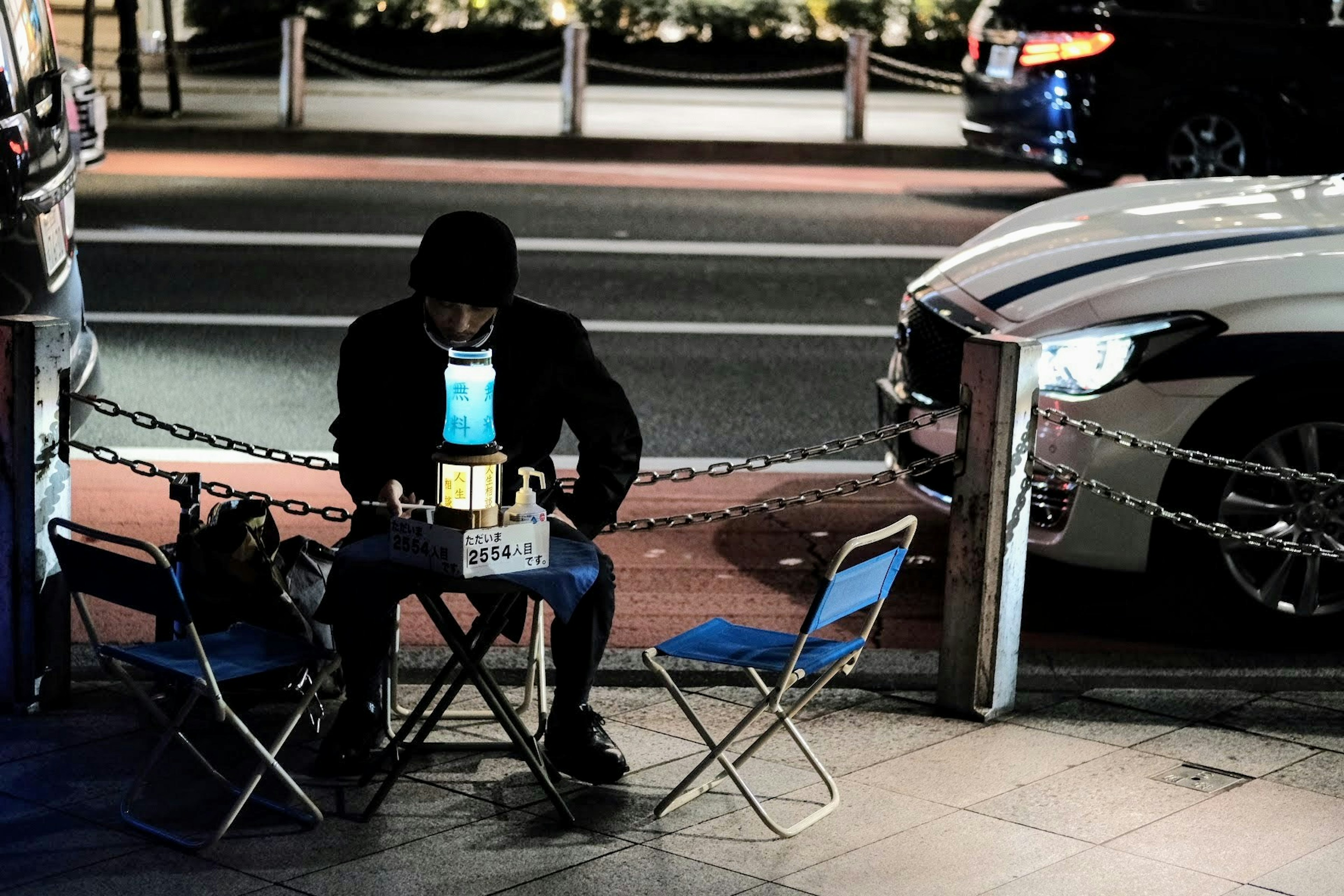 Uomo seduto di notte all'angolo della strada con un piccolo set di sedie