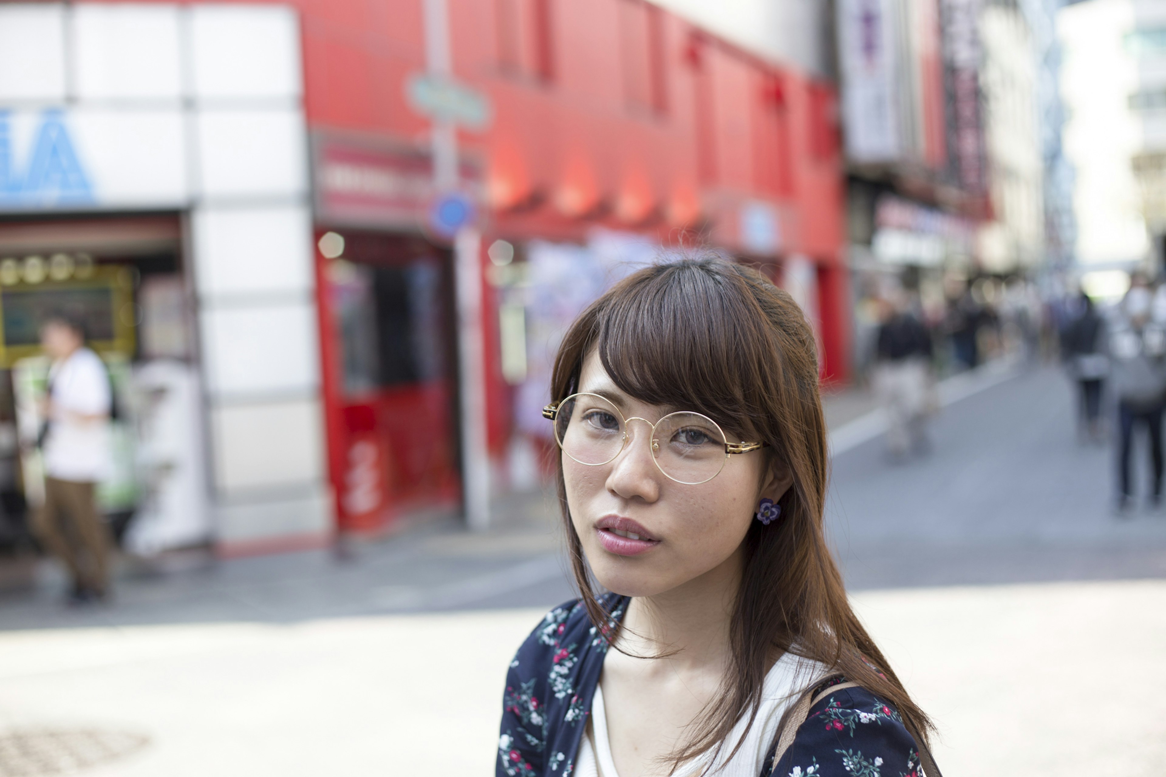 Una mujer mirando a la cámara en la calle con edificios rojos de fondo usando gafas