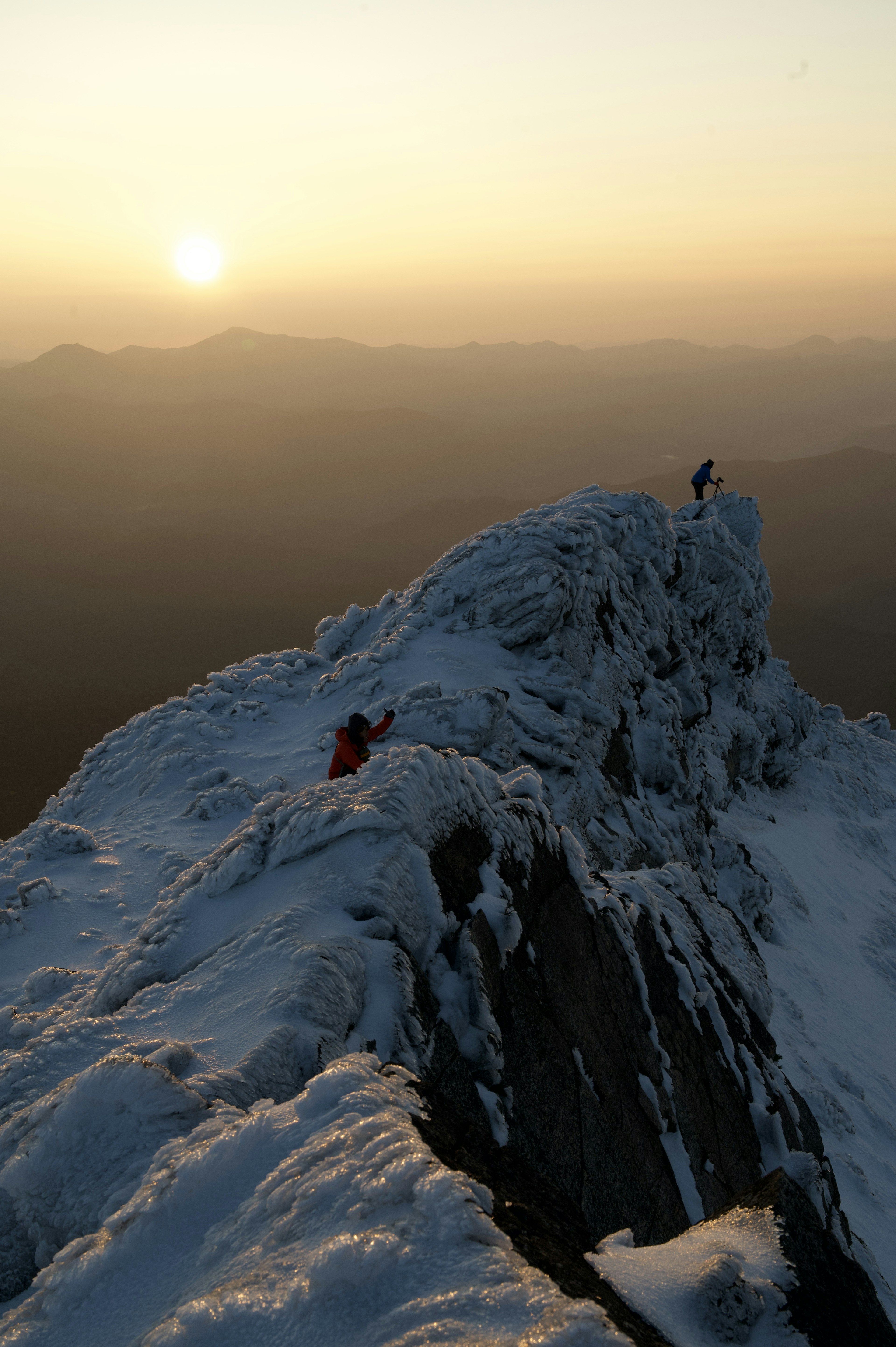 Climbers on a snowy mountain peak with a stunning sunset in the background