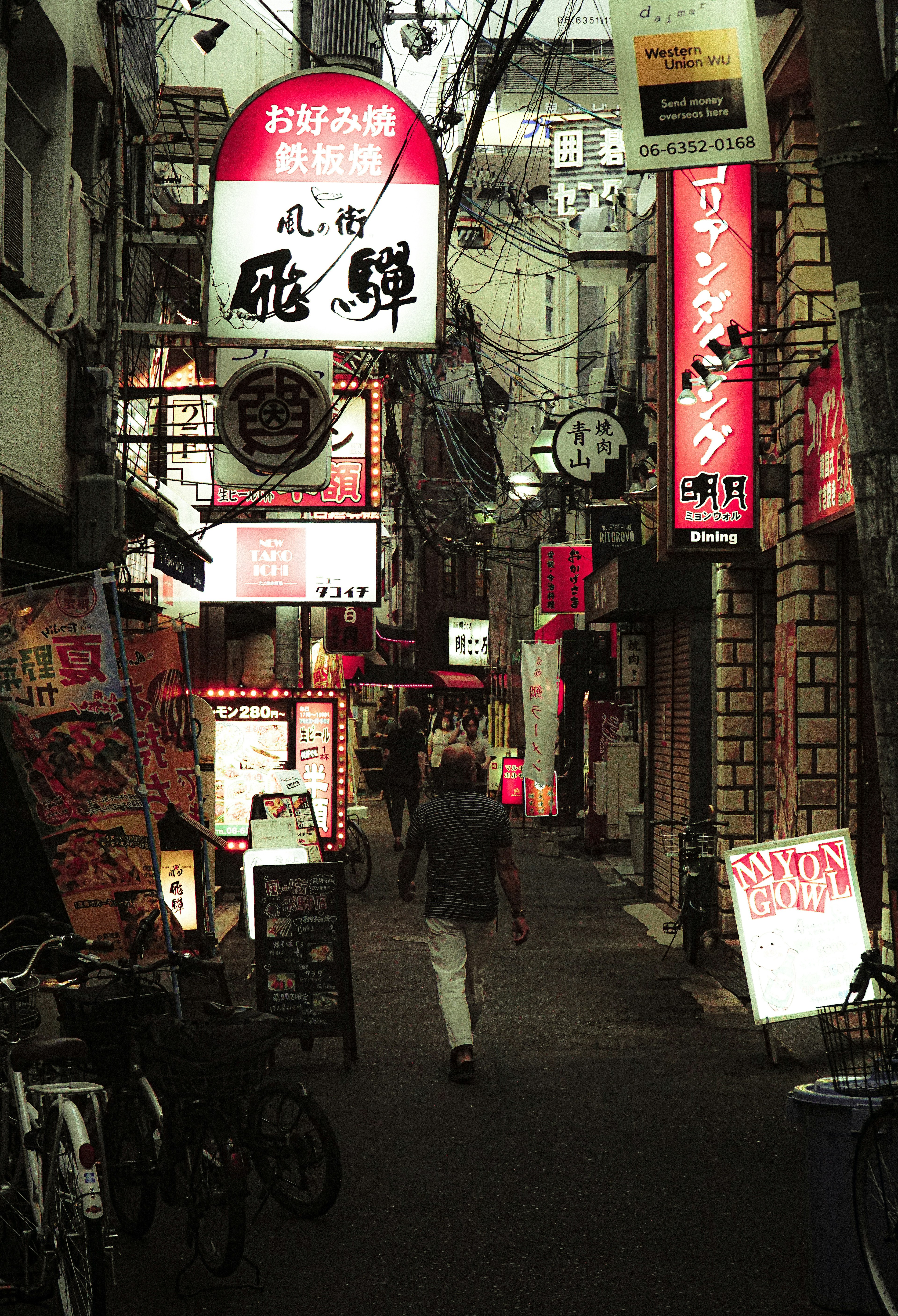 狭い路地に並ぶ明るいネオン看板と人が歩いている風景