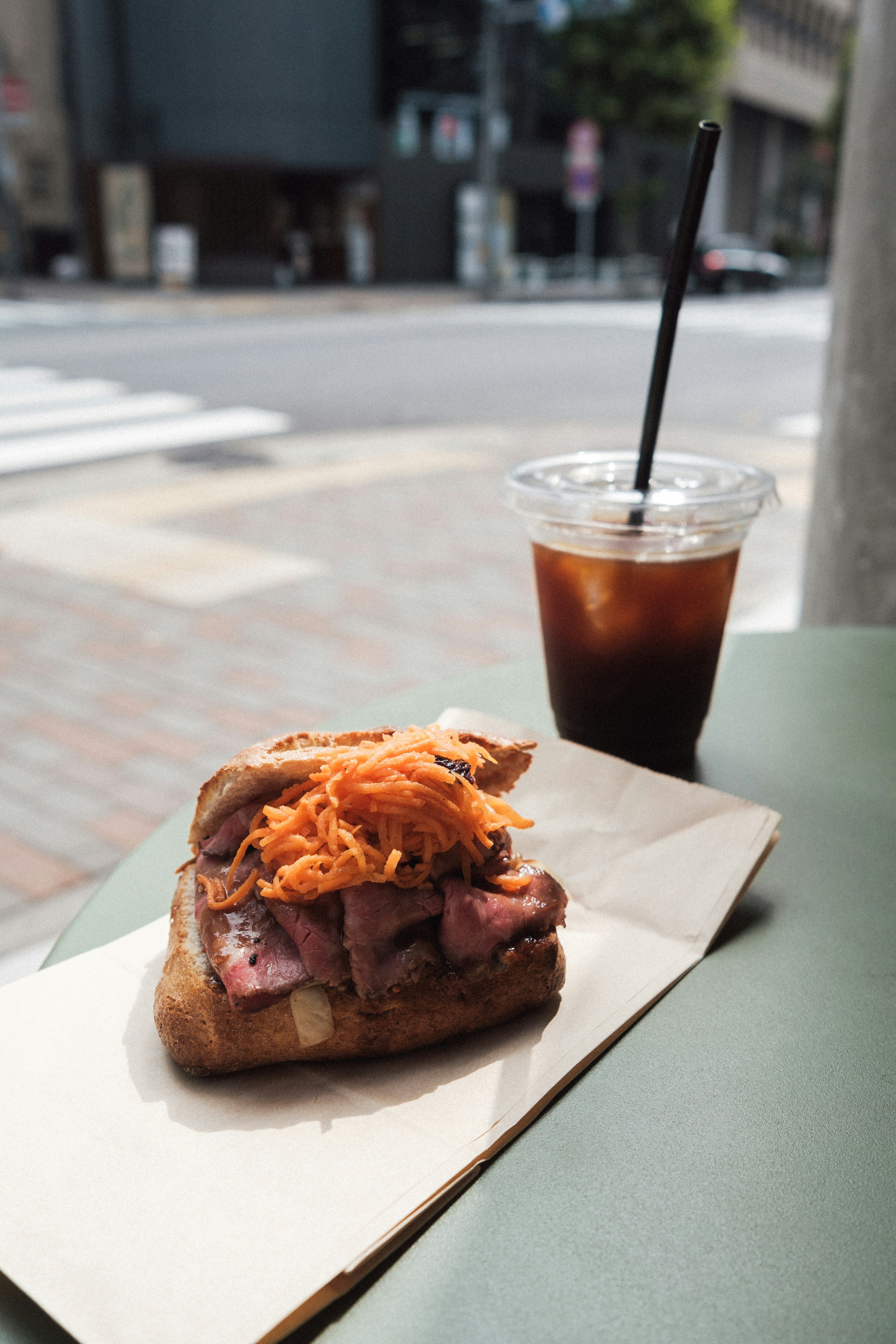 A sandwich with meat and vegetables next to an iced coffee on a table