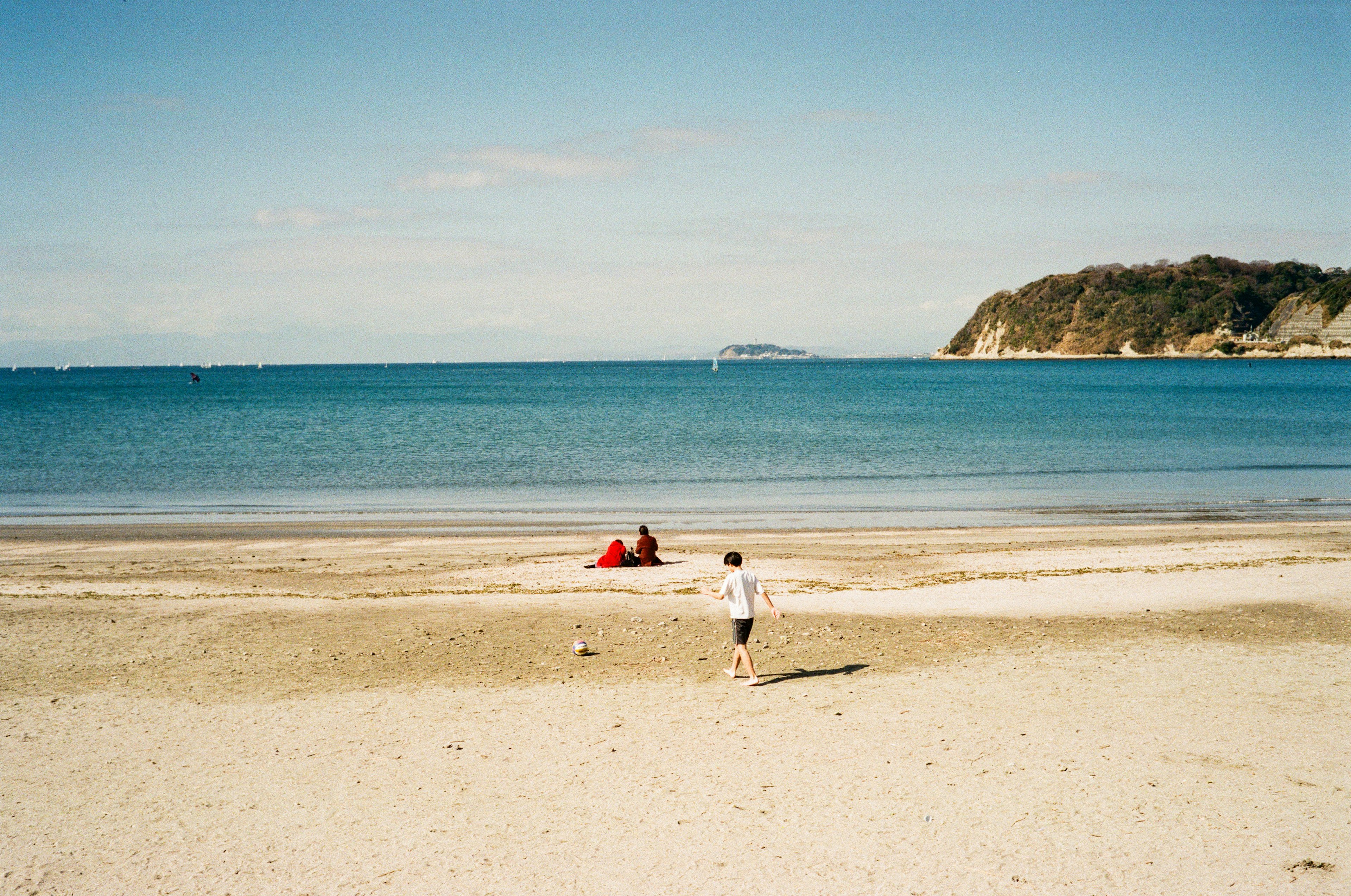 Enfant jouant sur une plage de sable avec un couple sur un tapis de plage rouge