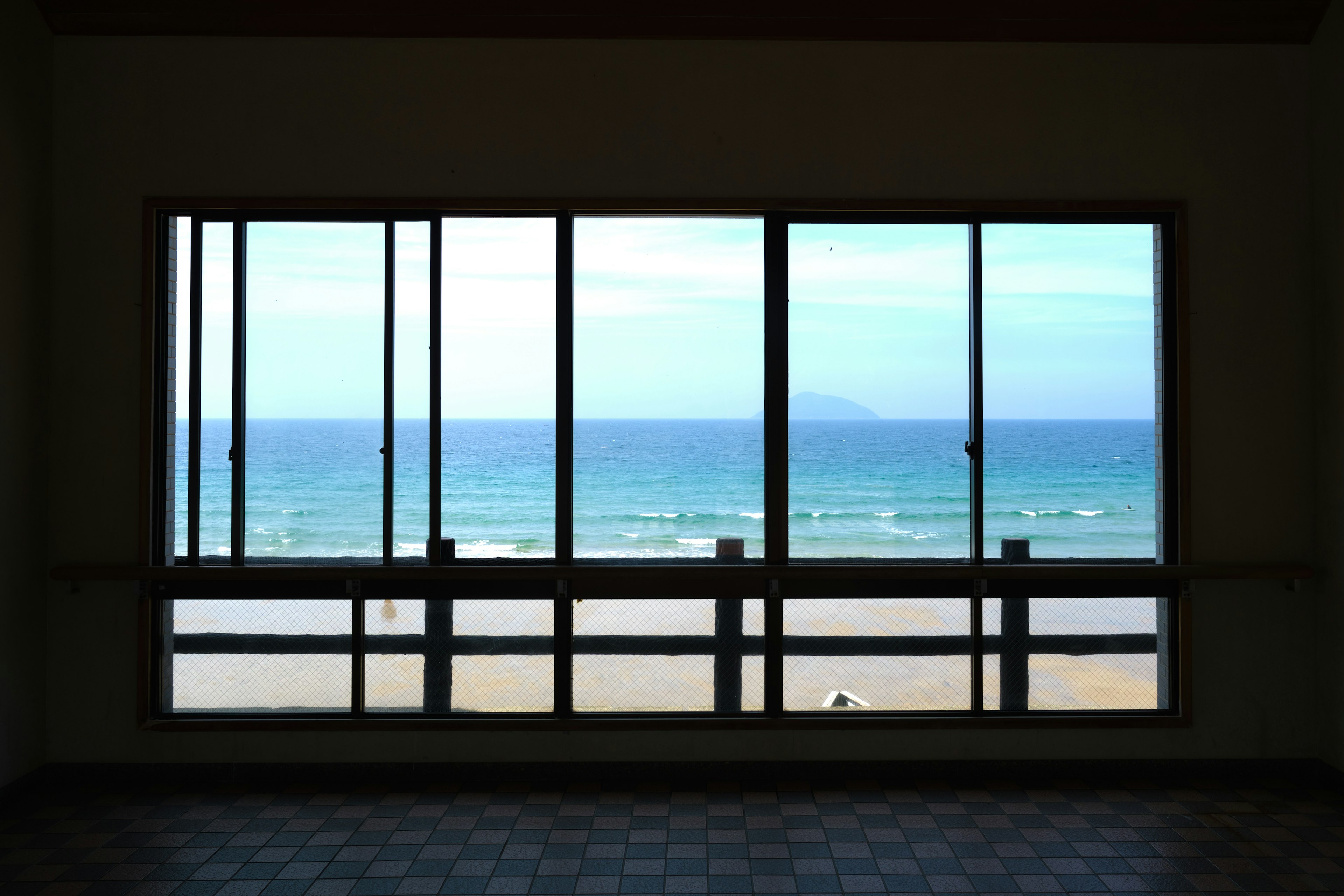 Innenansicht mit großen Fenstern, die einen Strand und den Ozean zeigen