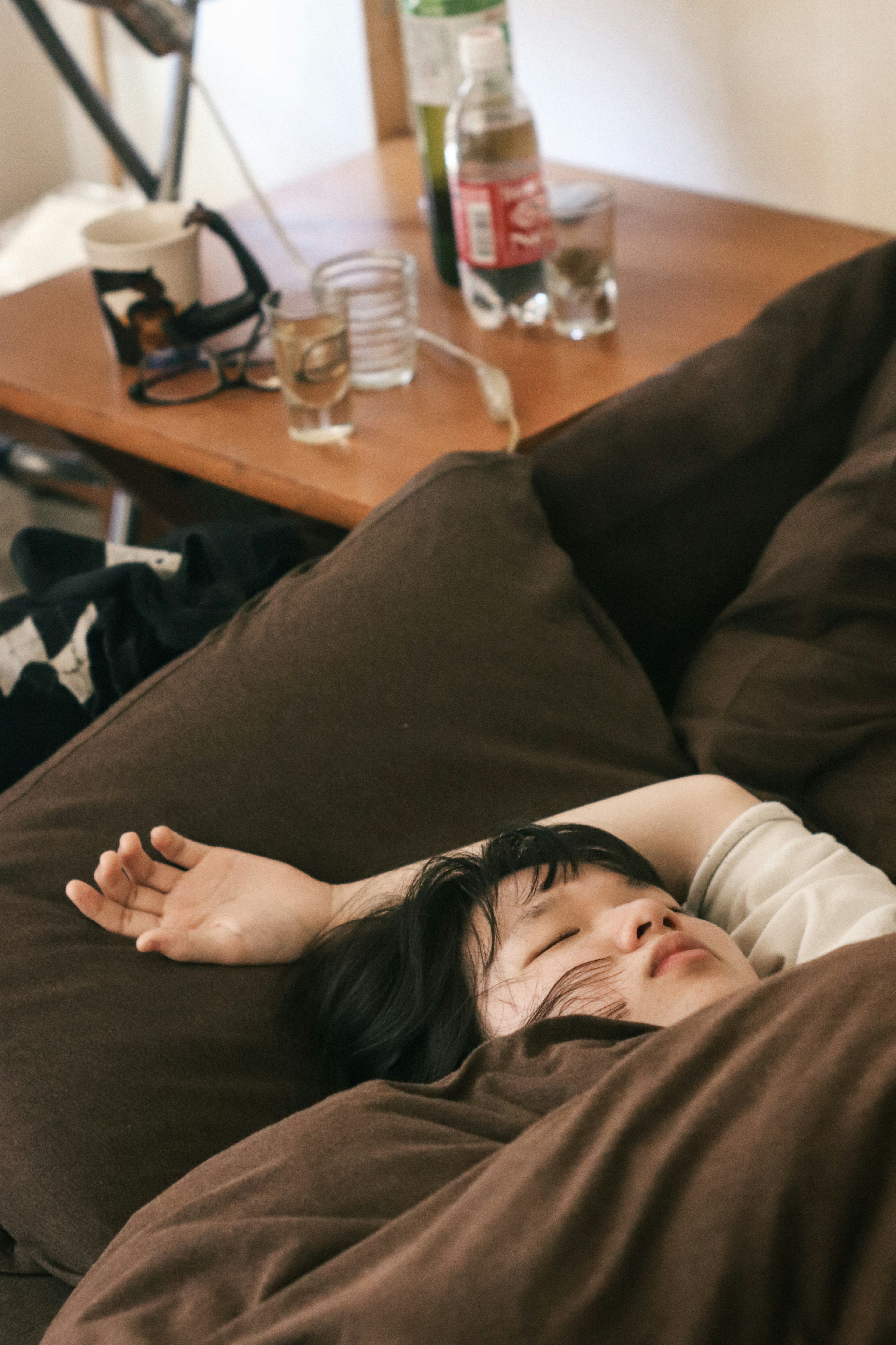 A woman sleeping on a bed surrounded by brown cushions and a wooden table