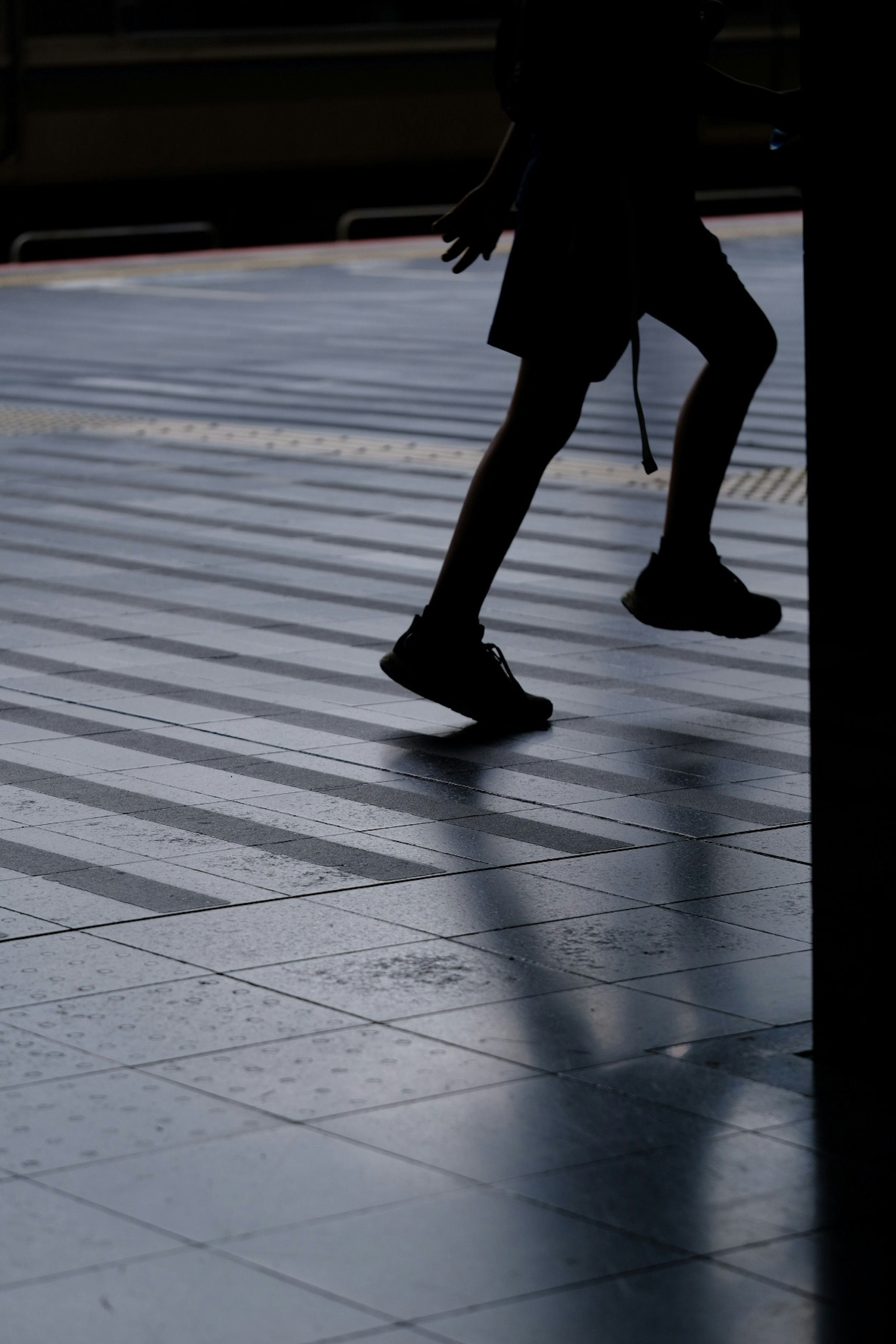 Silhouette di una persona che cammina su un pavimento piastrellato in una stazione