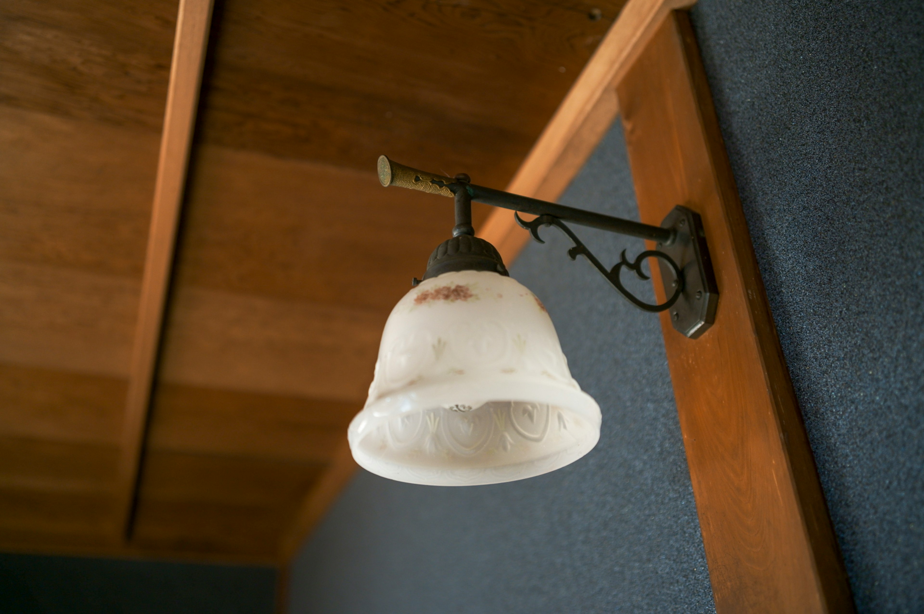 An old wall-mounted lamp with a white shade attached to a wooden wall