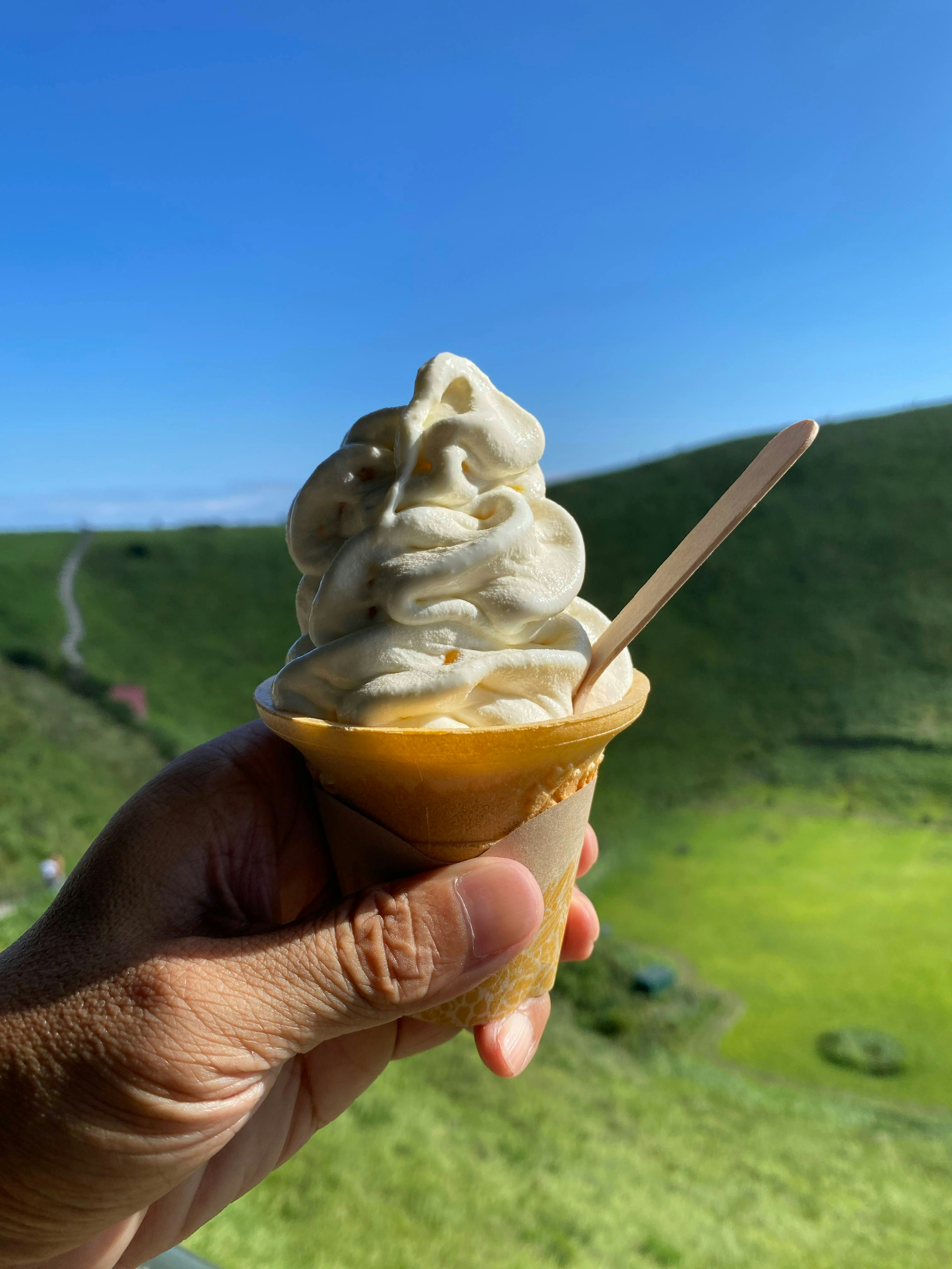 Mano che tiene un cono di gelato morbido con una collina verde sullo sfondo